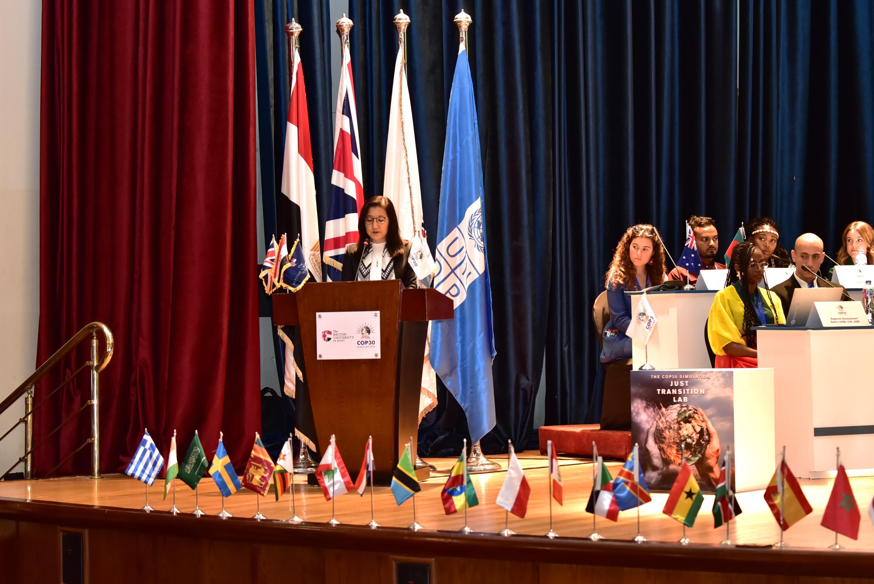 Conference stage with podium, a row of national flags, and a panel of speakers.