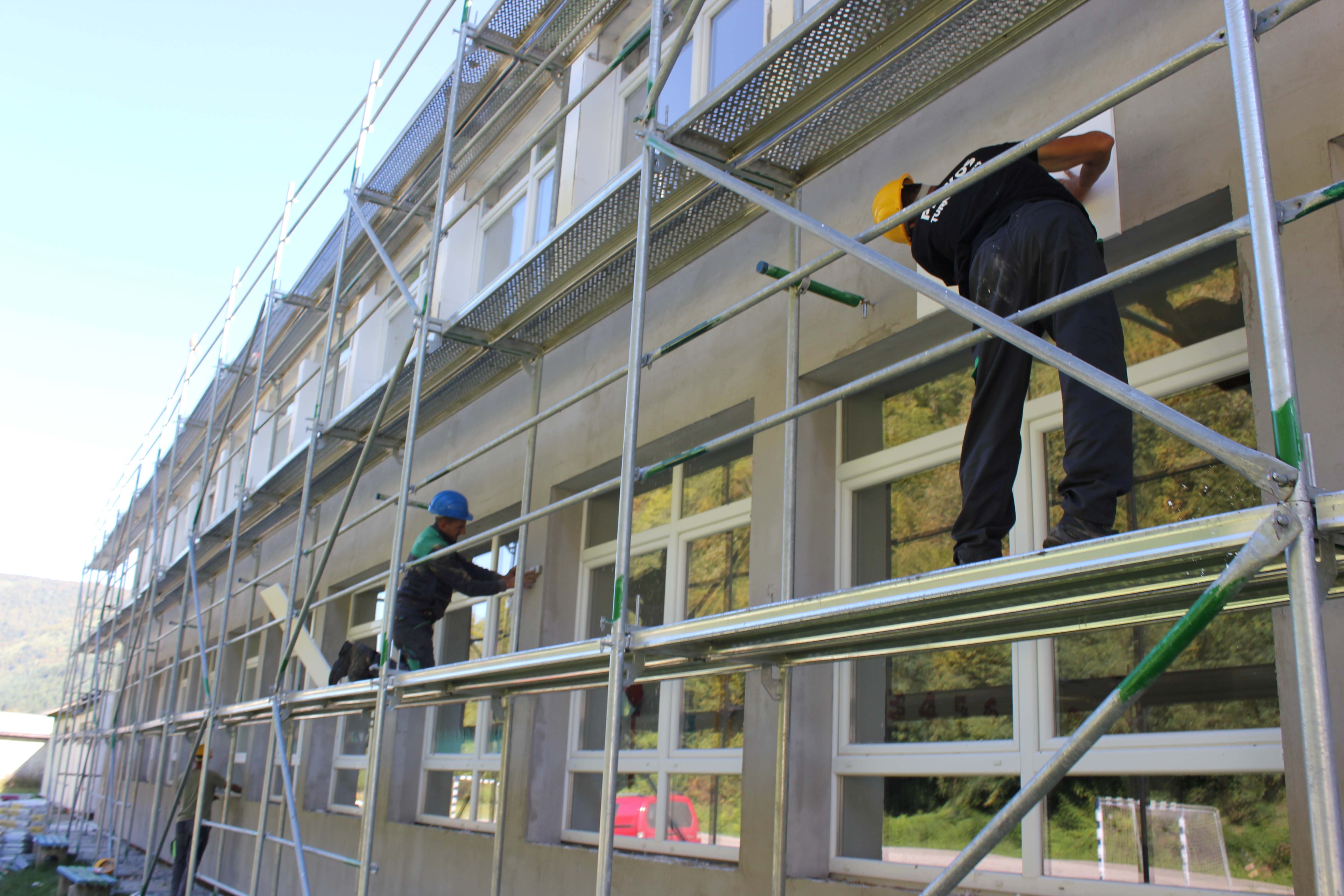 Several construction workers on scaffolding around a beige building.