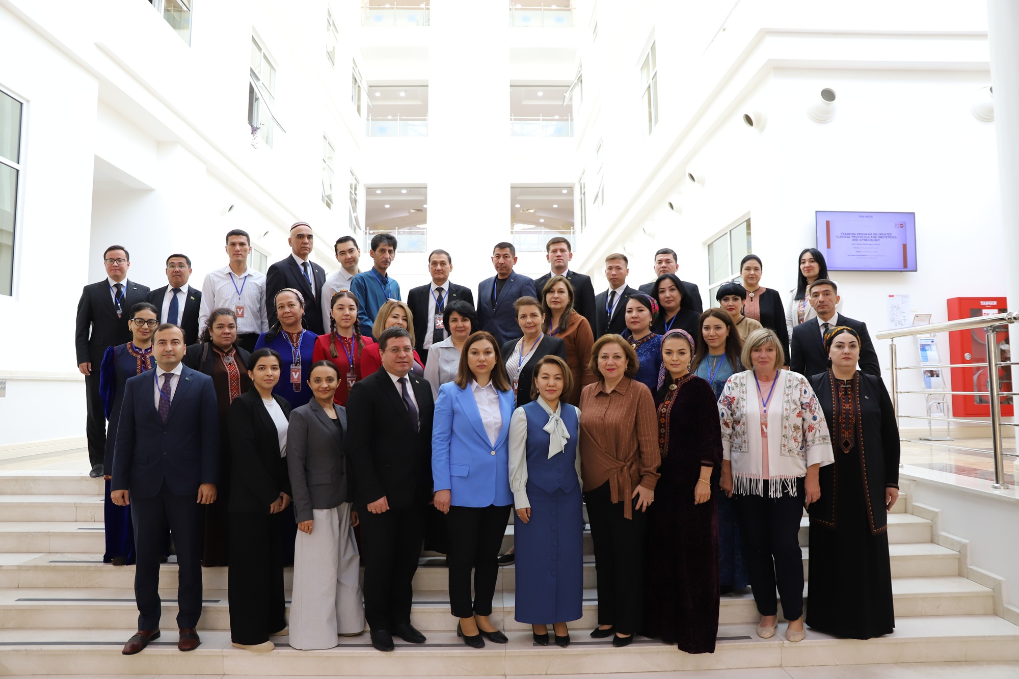 Group photograph of diverse professionals posing on a staircase in a bright atrium.