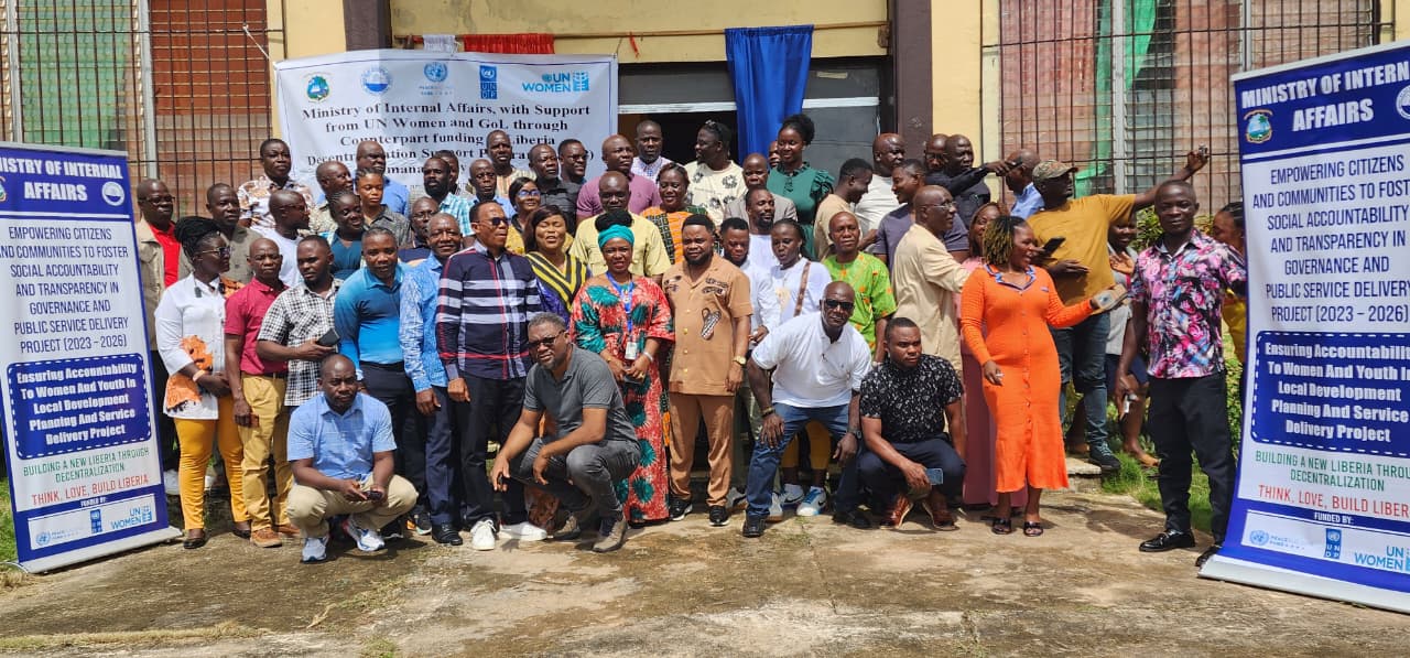 Photograph of a large group posing outdoors at a community event with banners.
