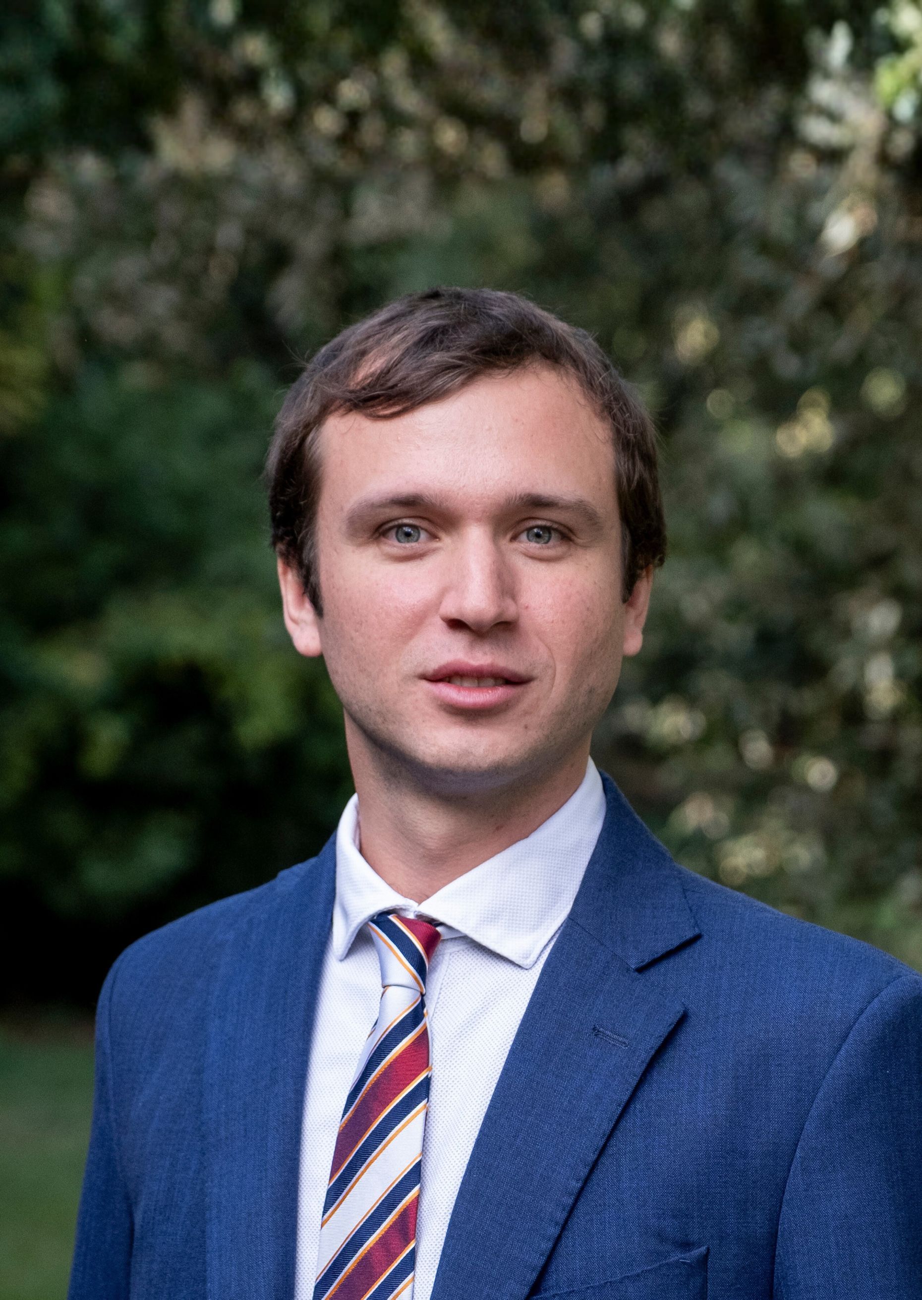 Portrait of a man in a blue suit with a striped tie outdoors.
