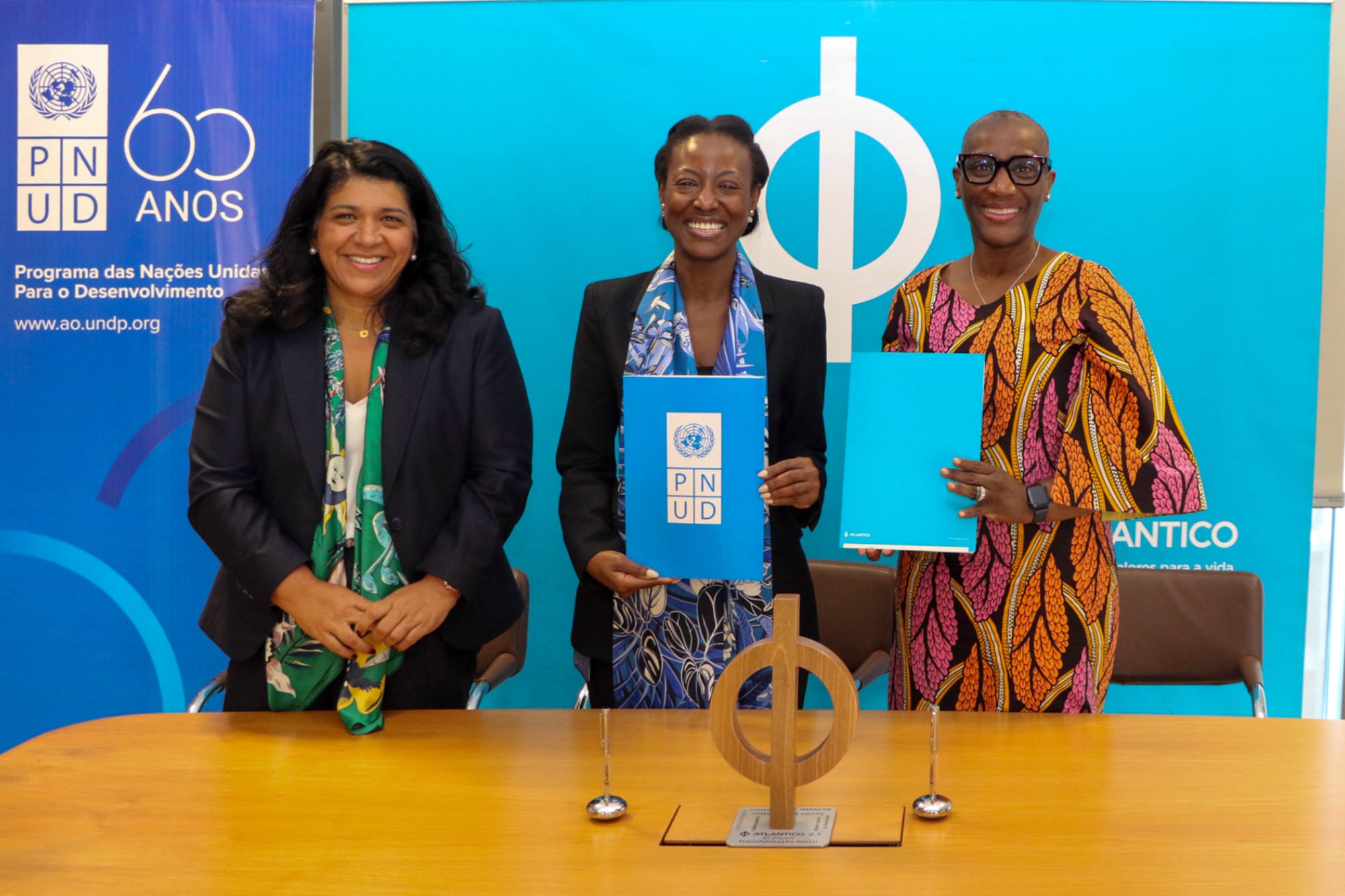 Four people pose behind a wooden table at a blue backdrop; two hold blue signs.