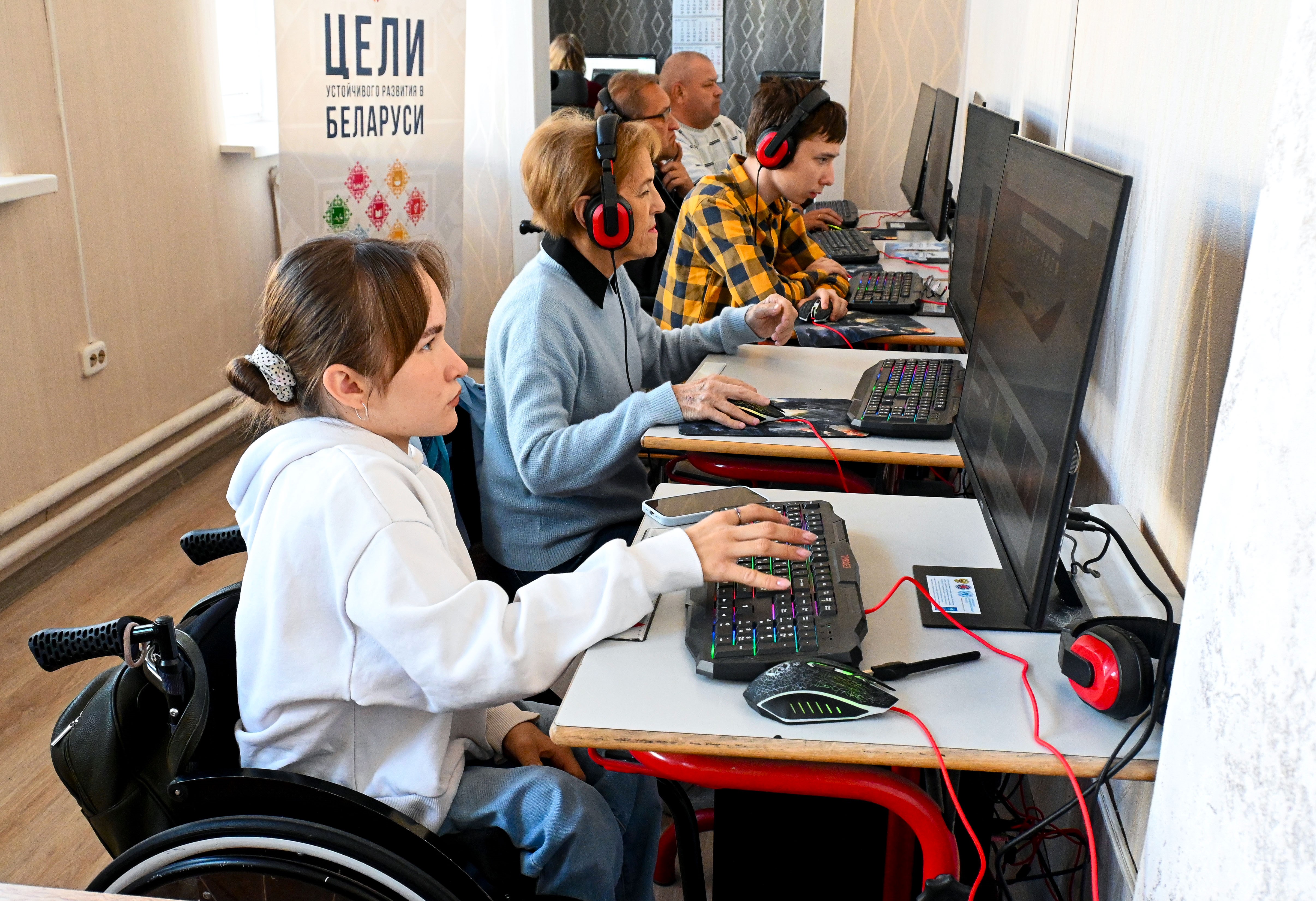 Photo of students at desks with computers and headphones in a classroom; wheelchair user in front.