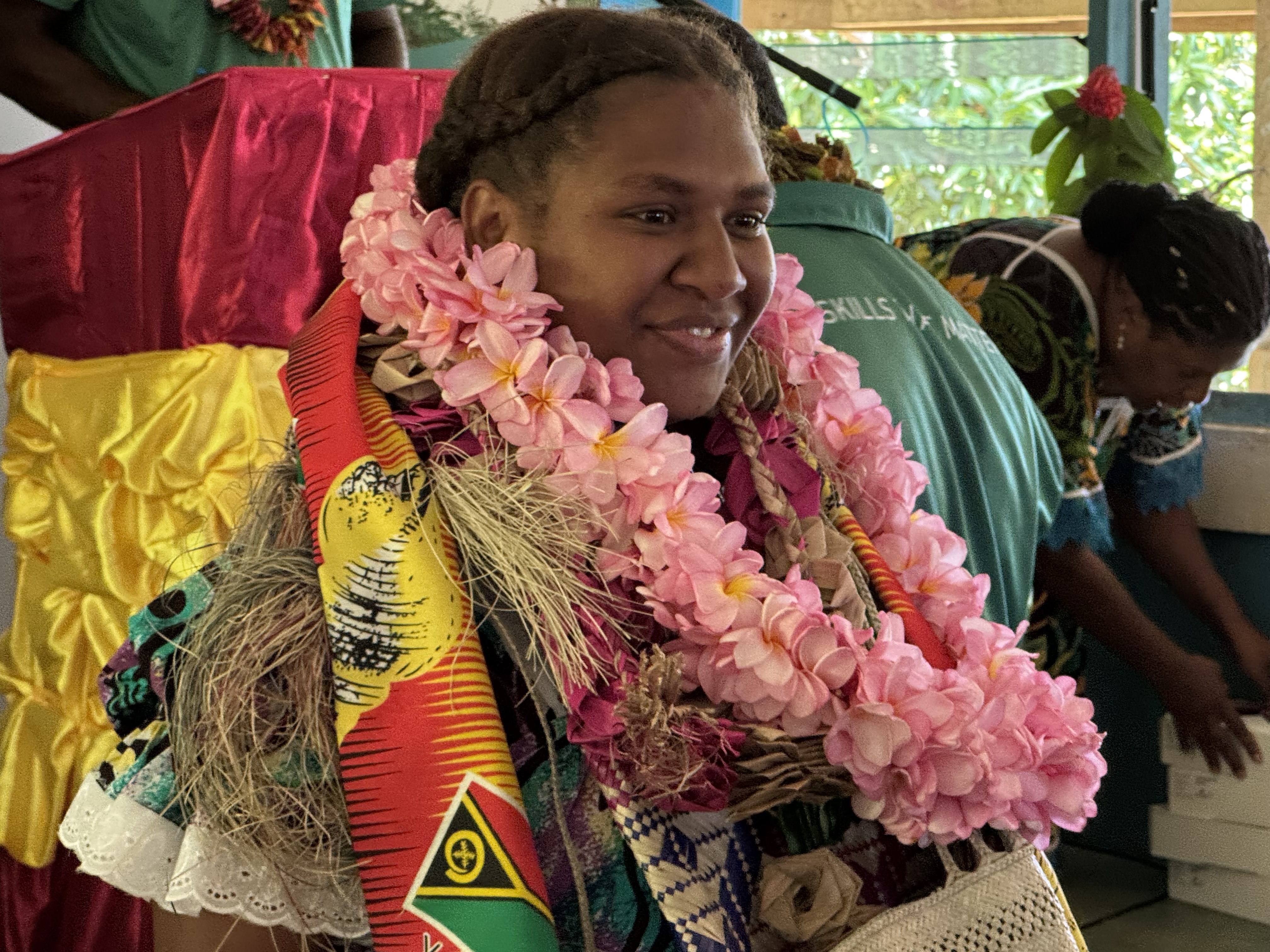 Person wearing pink flower leis at a colorful outdoor festival.
