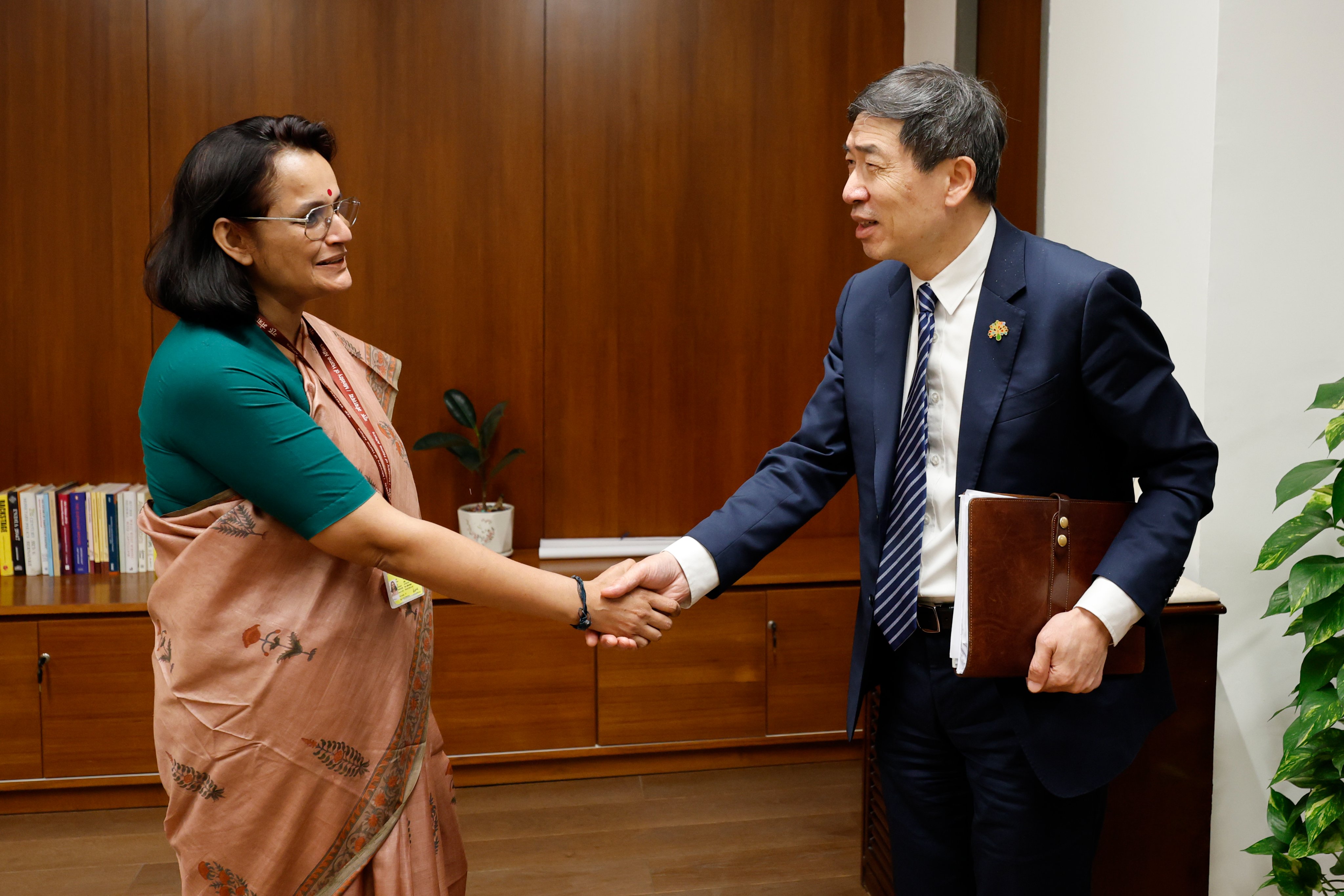 Woman in green blouse and brown sari shakes hands with a suited man in an office.