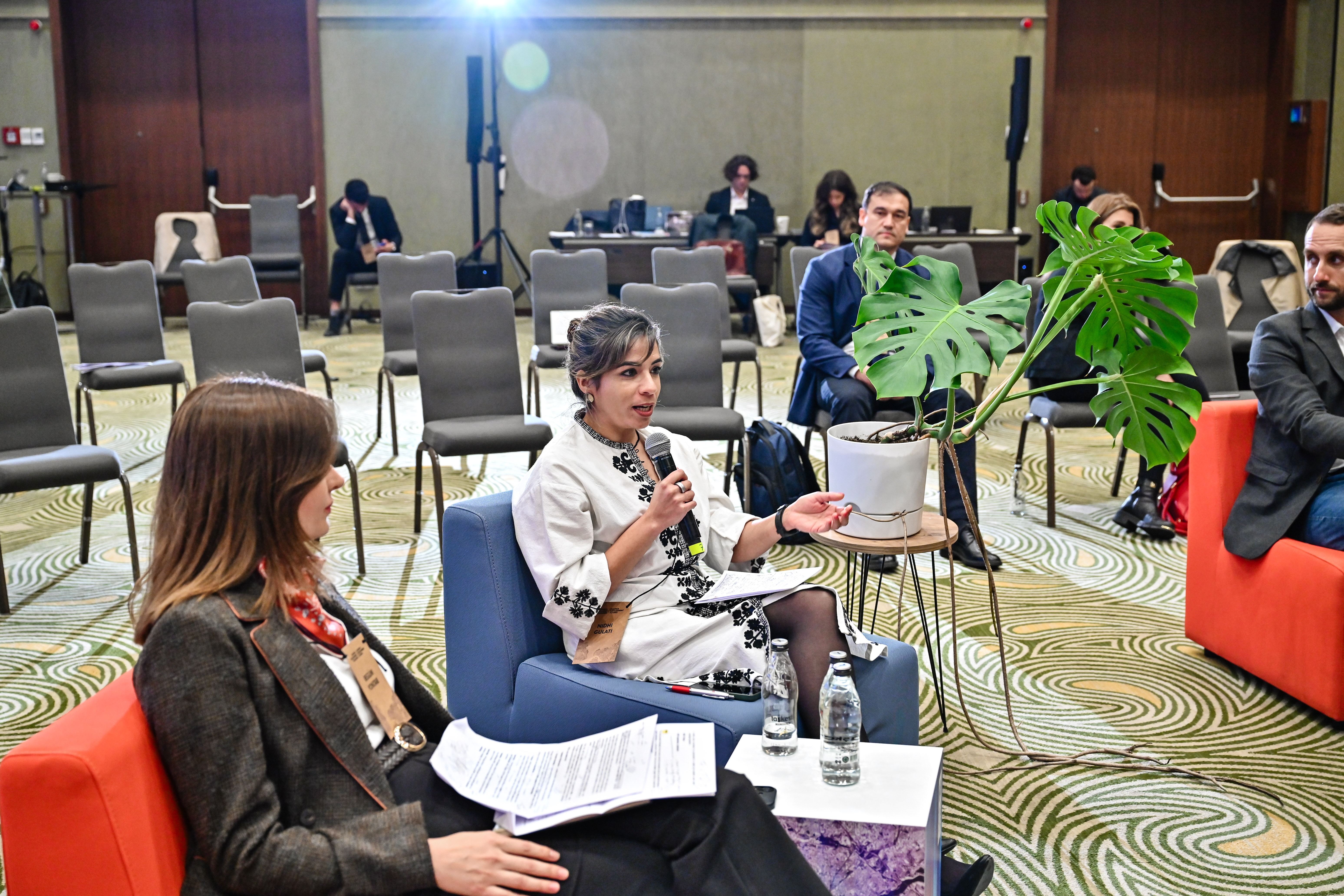 Photo: Panel discussion at a conference with people seated in foreground and a plant on the table.