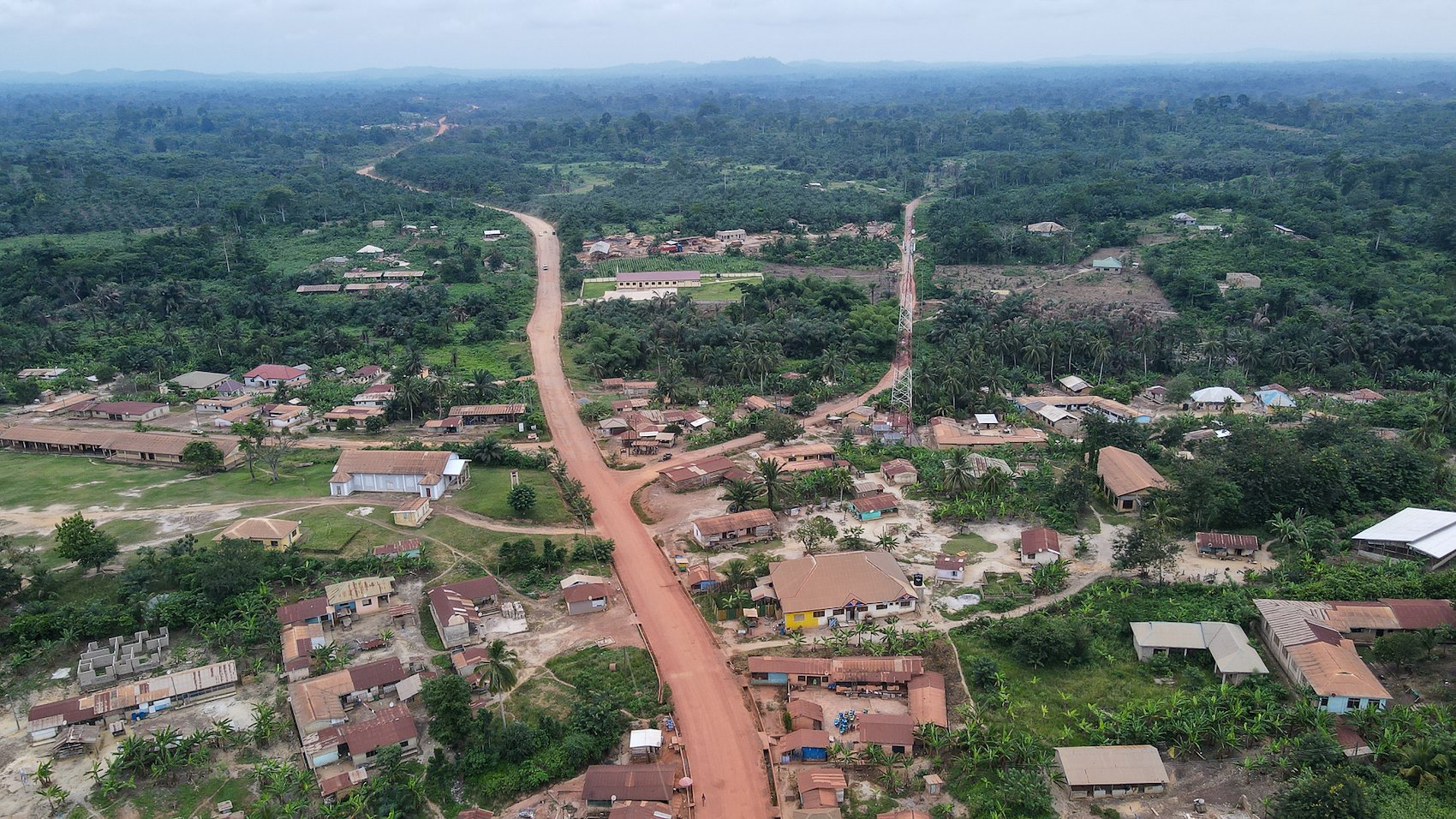 Aerial photo of a rural village with a winding red dirt road through green fields.