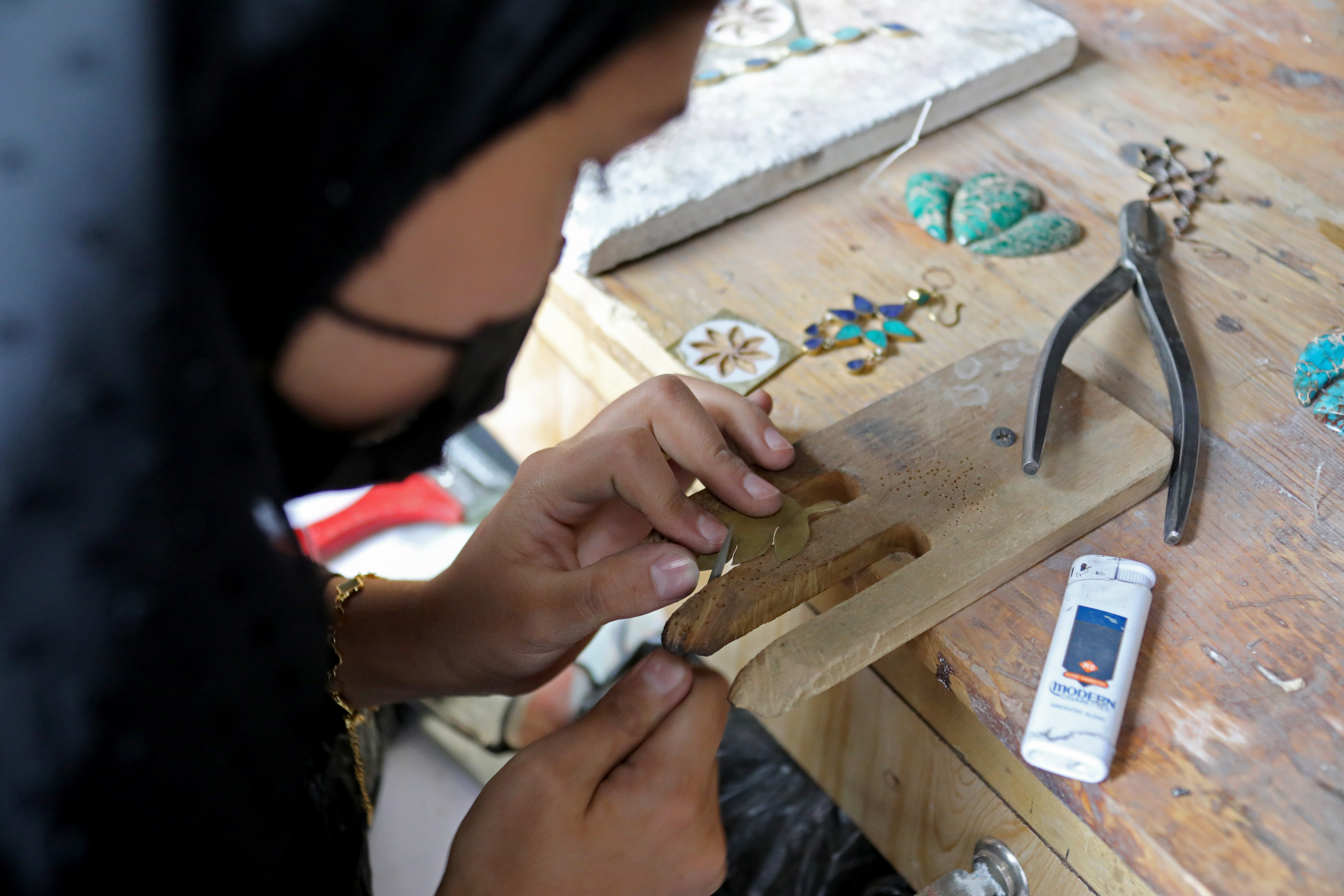 Hands cutting brown leather on a wooden workbench with tools and a smartphone nearby.