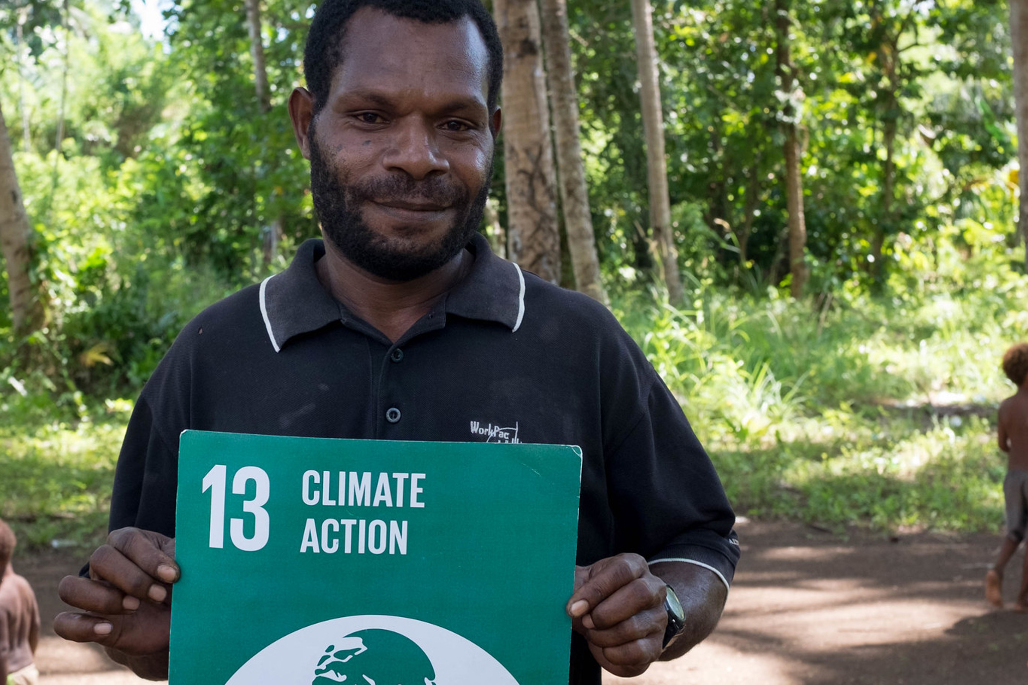 Man holding a Climate Action sign with a globe icon in a sunlit forest.