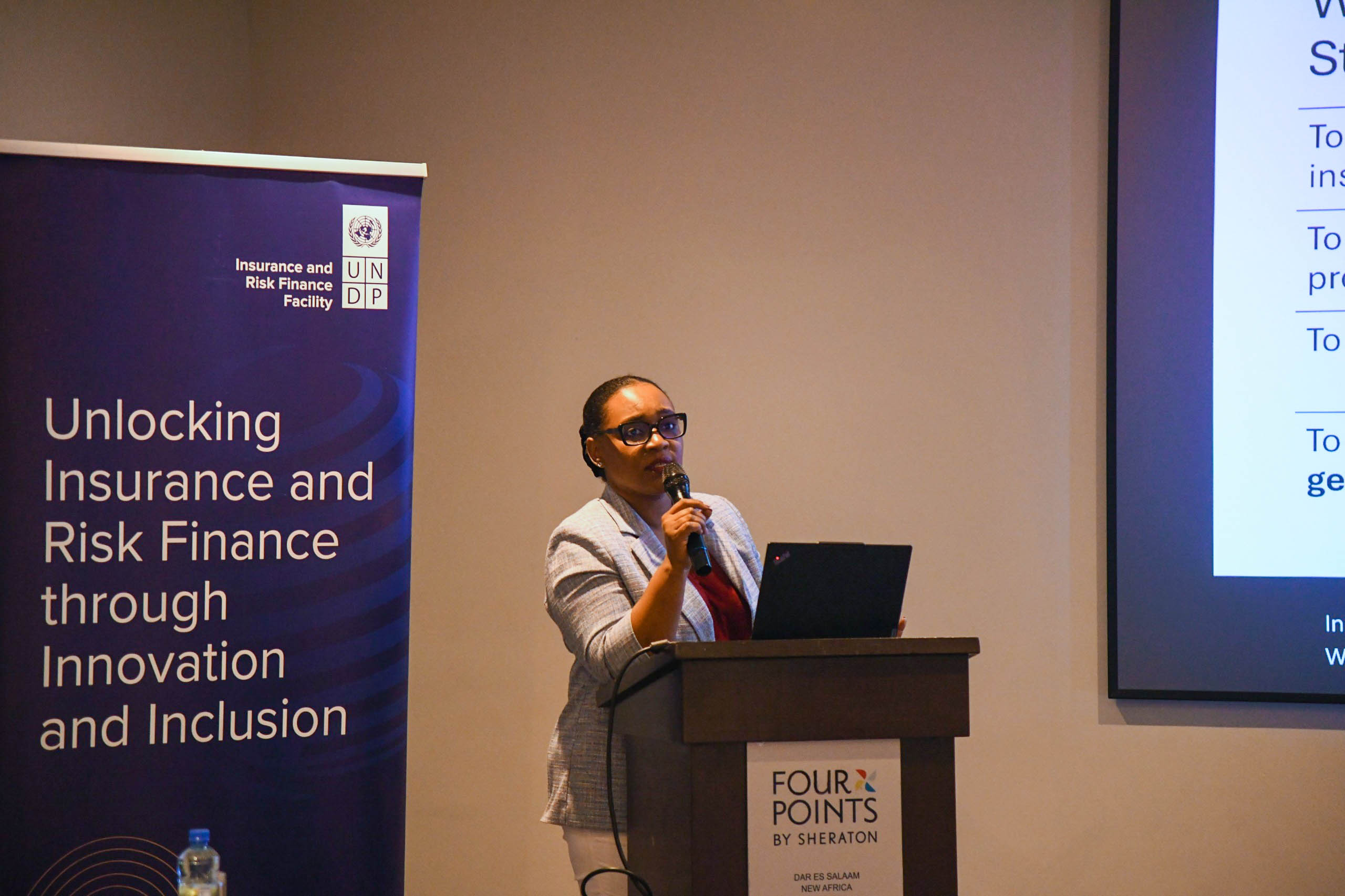 Man giving a talk at a podium beside a purple banner about unlocking insurance and risk finance.