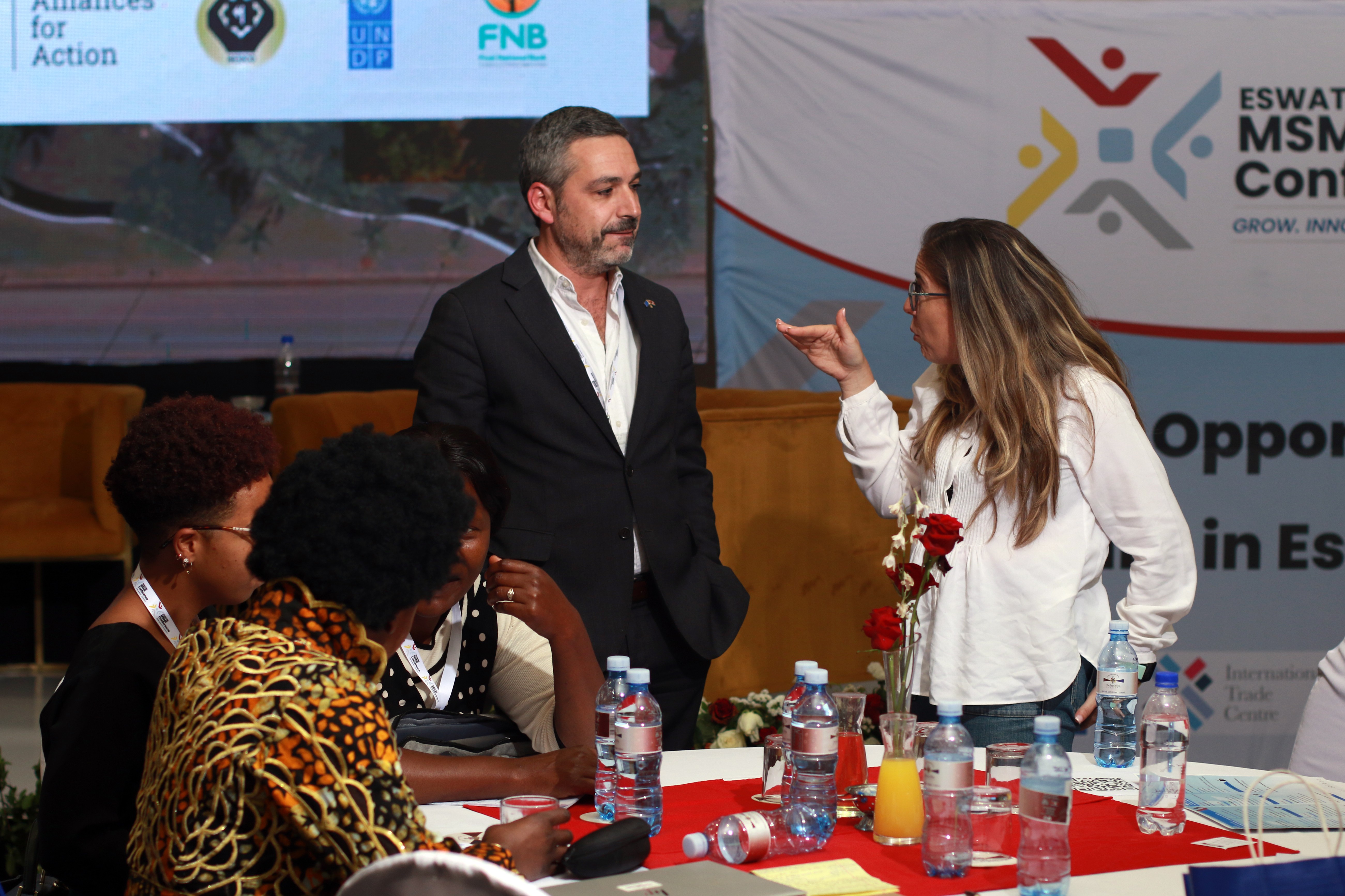 Photograph: award ceremony with a man presenting trophies to a woman at a table.