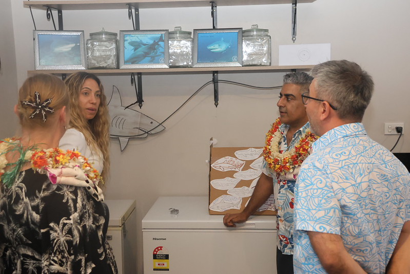 Four adults in a classroom listening to a presenter beside a curved skeletal model.