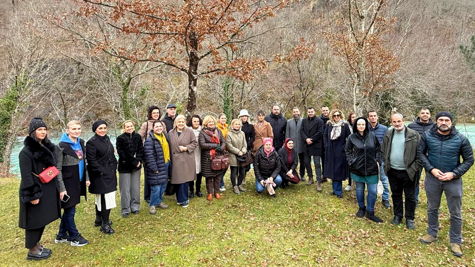 Group of people in coats posing outdoors in a fall park with orange-leaved trees.