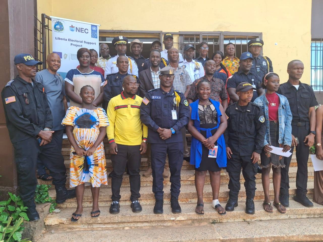 Group photo of community members and uniformed officers outside a yellow building.