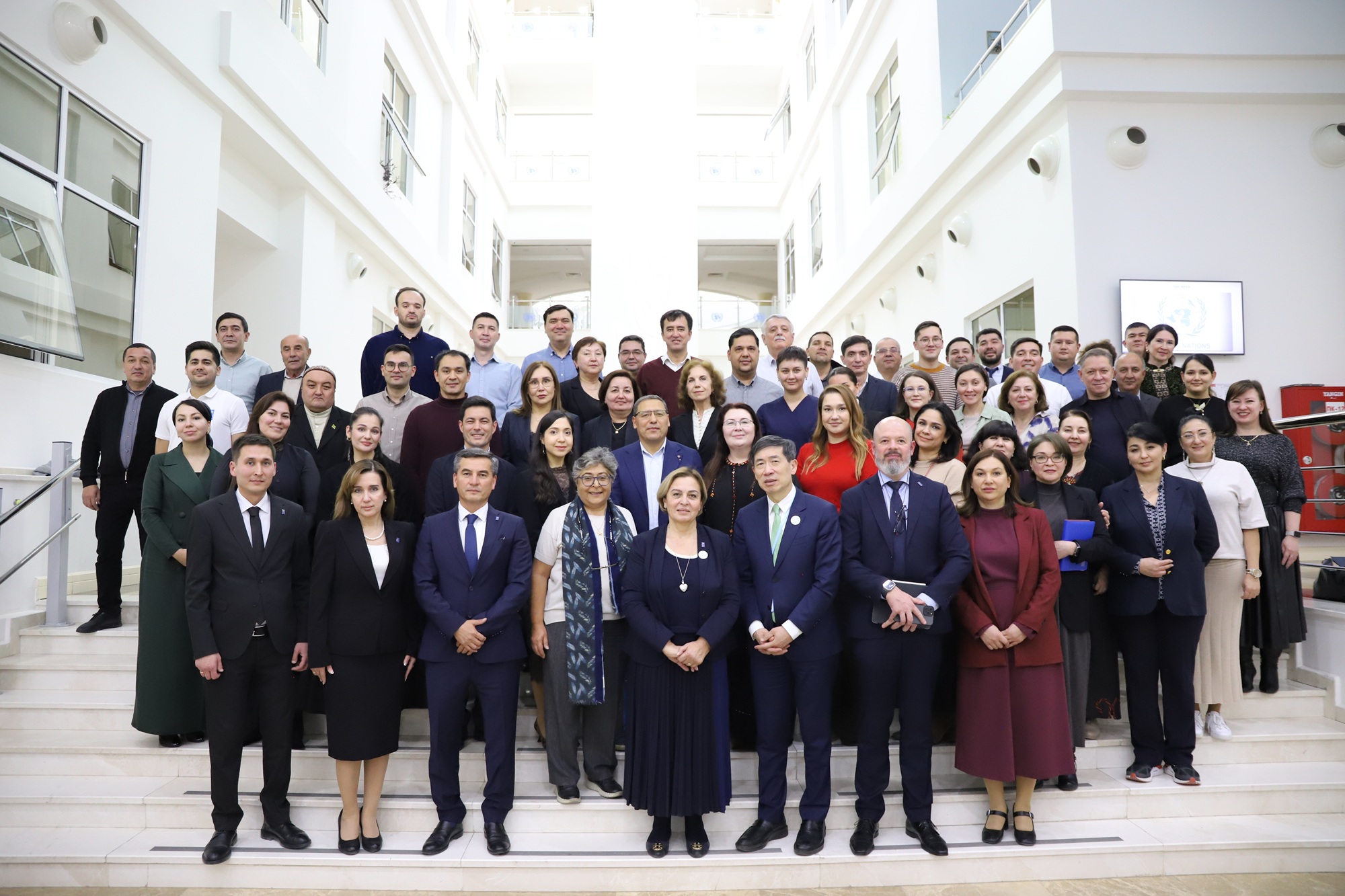 Group of diverse professionals in formal attire posing on white steps in a bright courtyard.