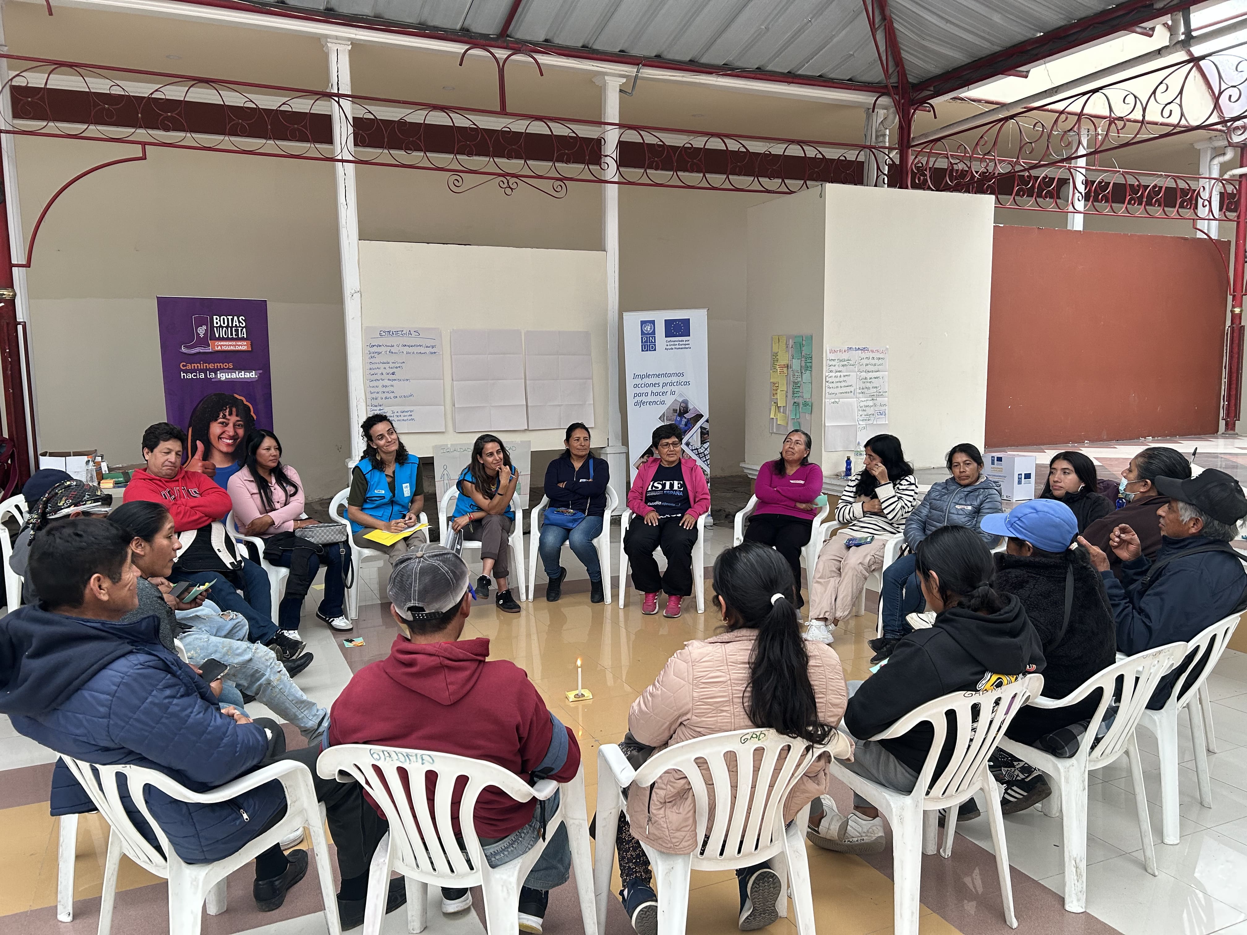 Group of people seated in a circle under a covered patio during a community workshop.