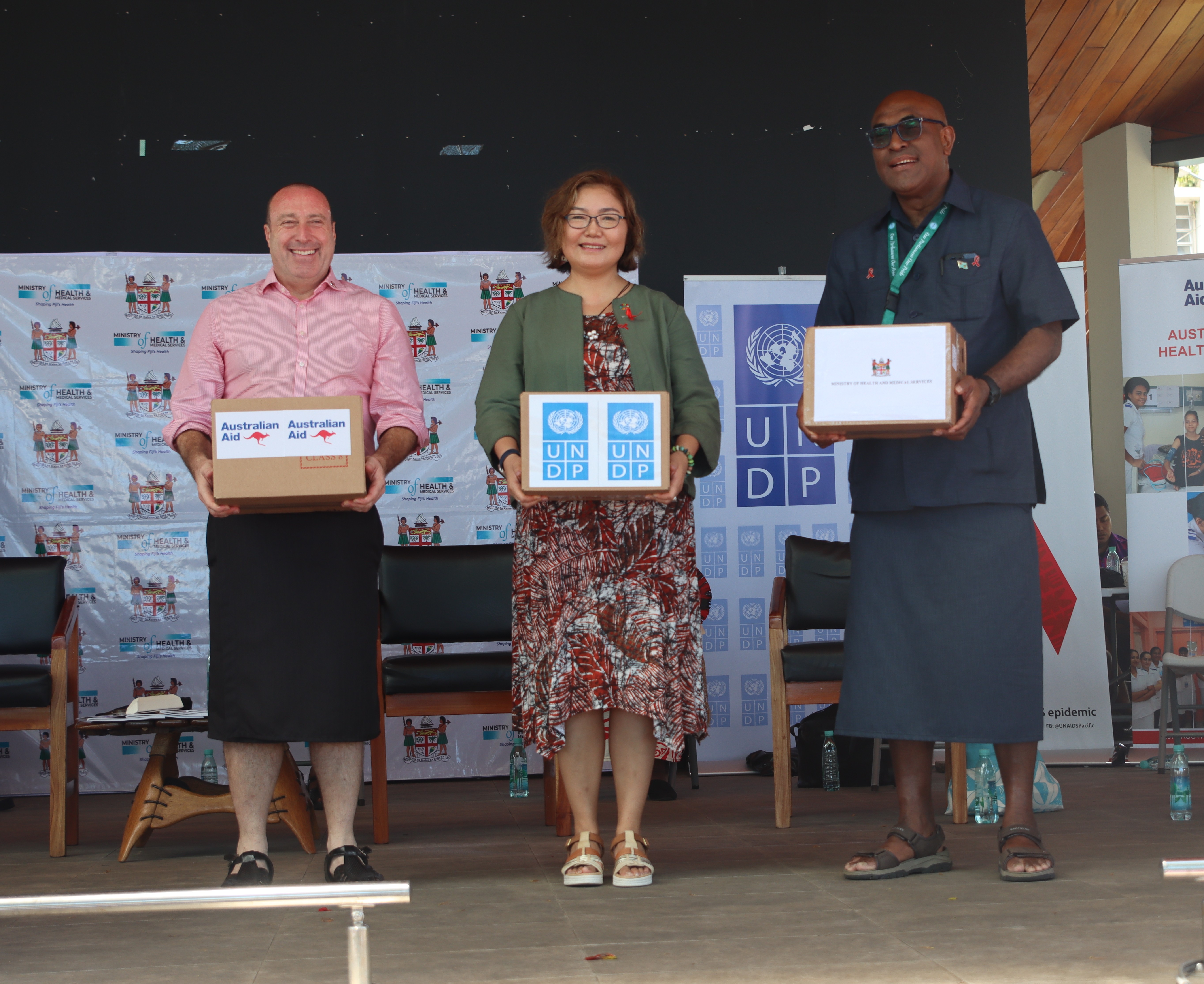 Three people on stage holding certificates at an awards ceremony, banner in the background.
