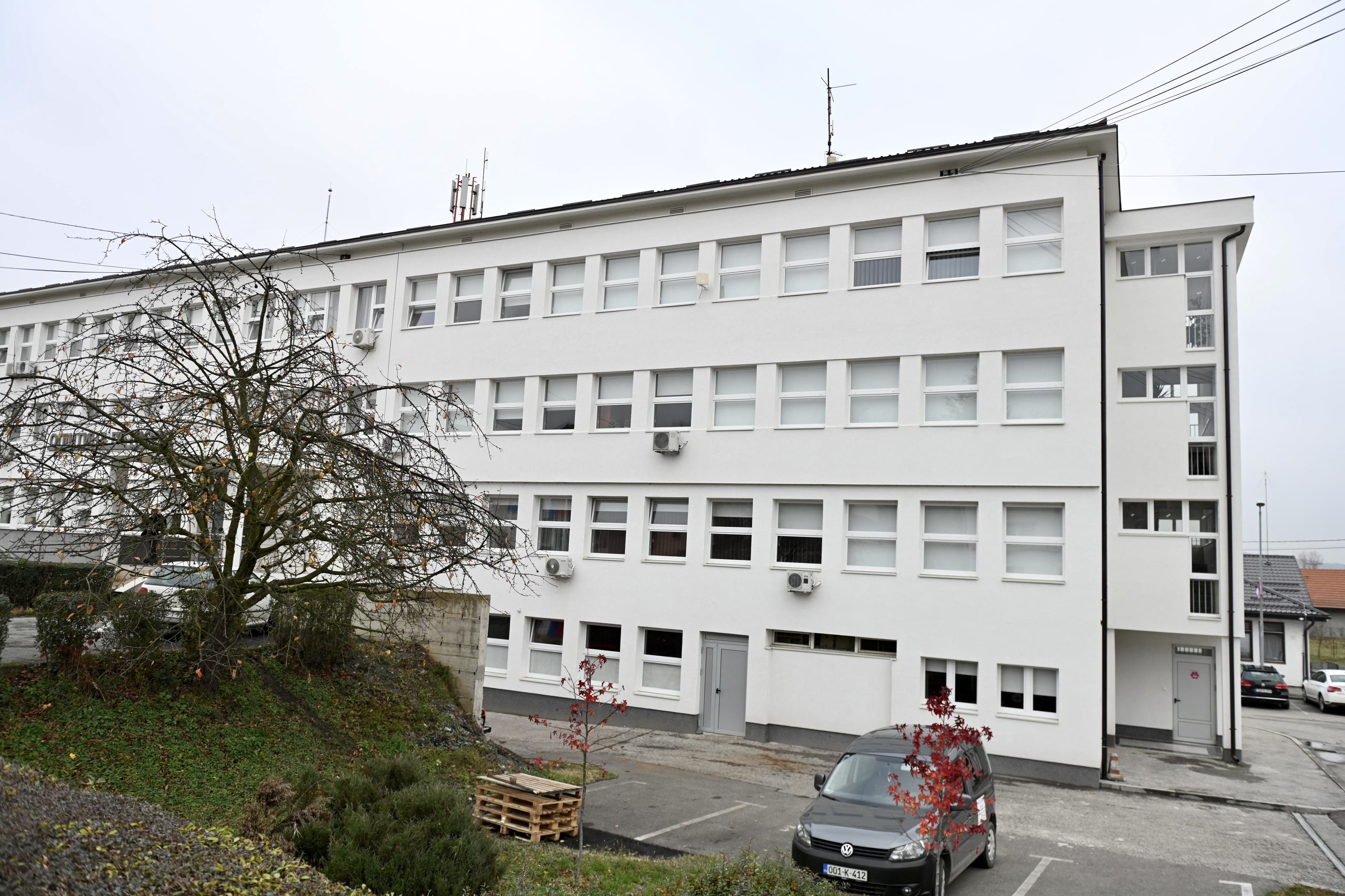 Photograph of a white, multi-story building with many windows, a small yard, and a parked car.