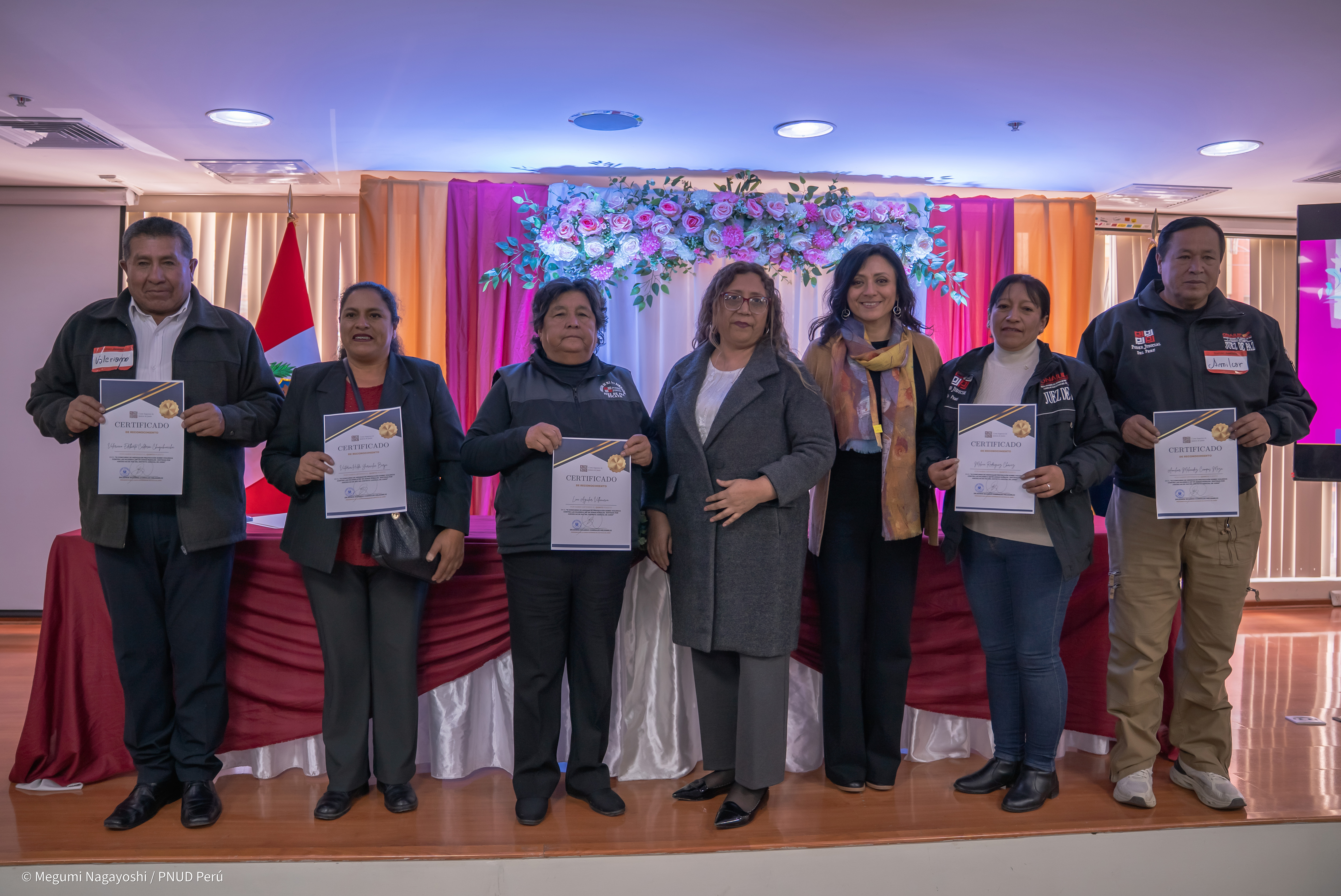 Group of people on a stage holding certificates during an award ceremony, colorful backdrop.
