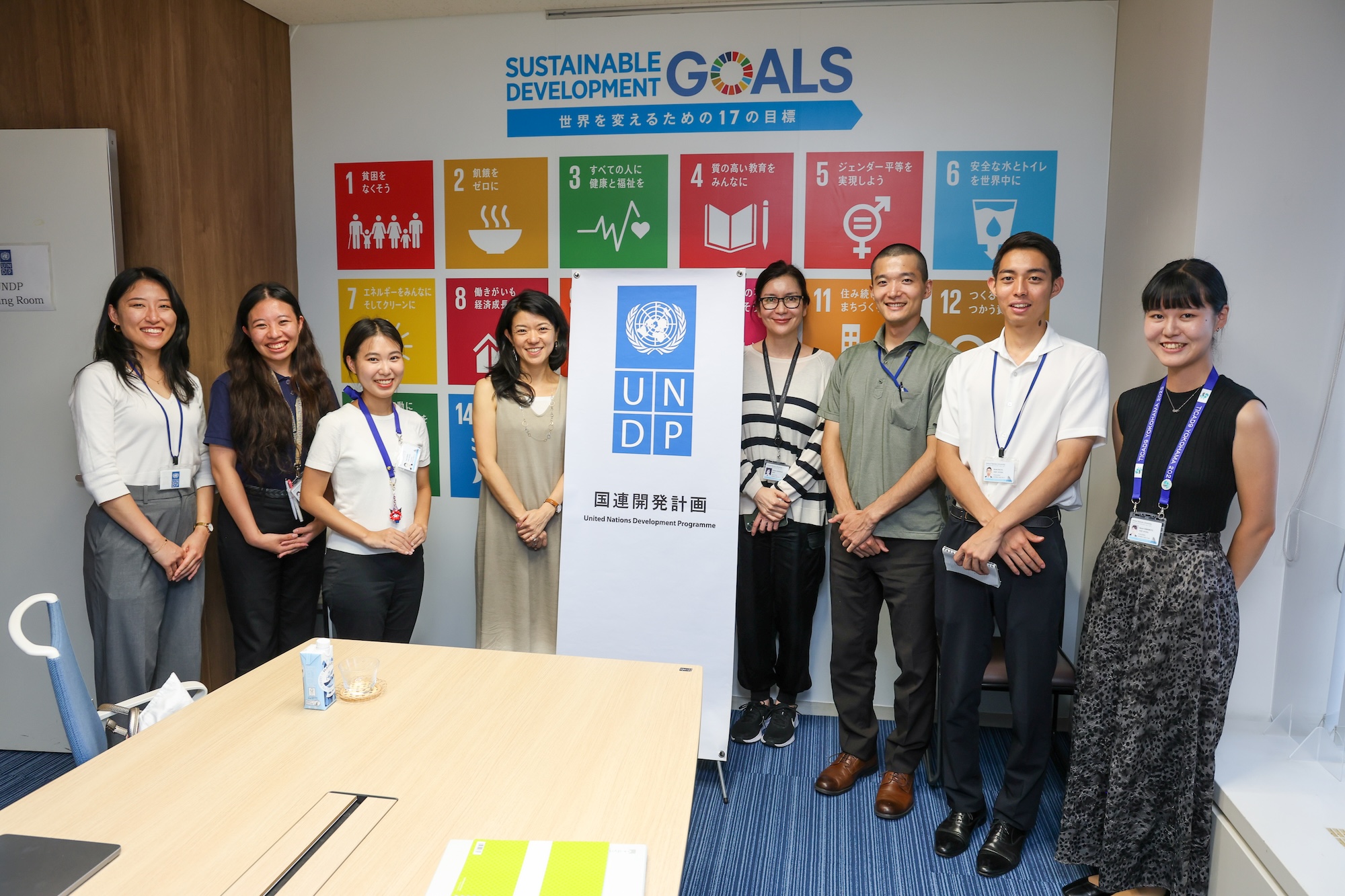 Group of professionals standing in a conference room around a banner displaying SDG icons.