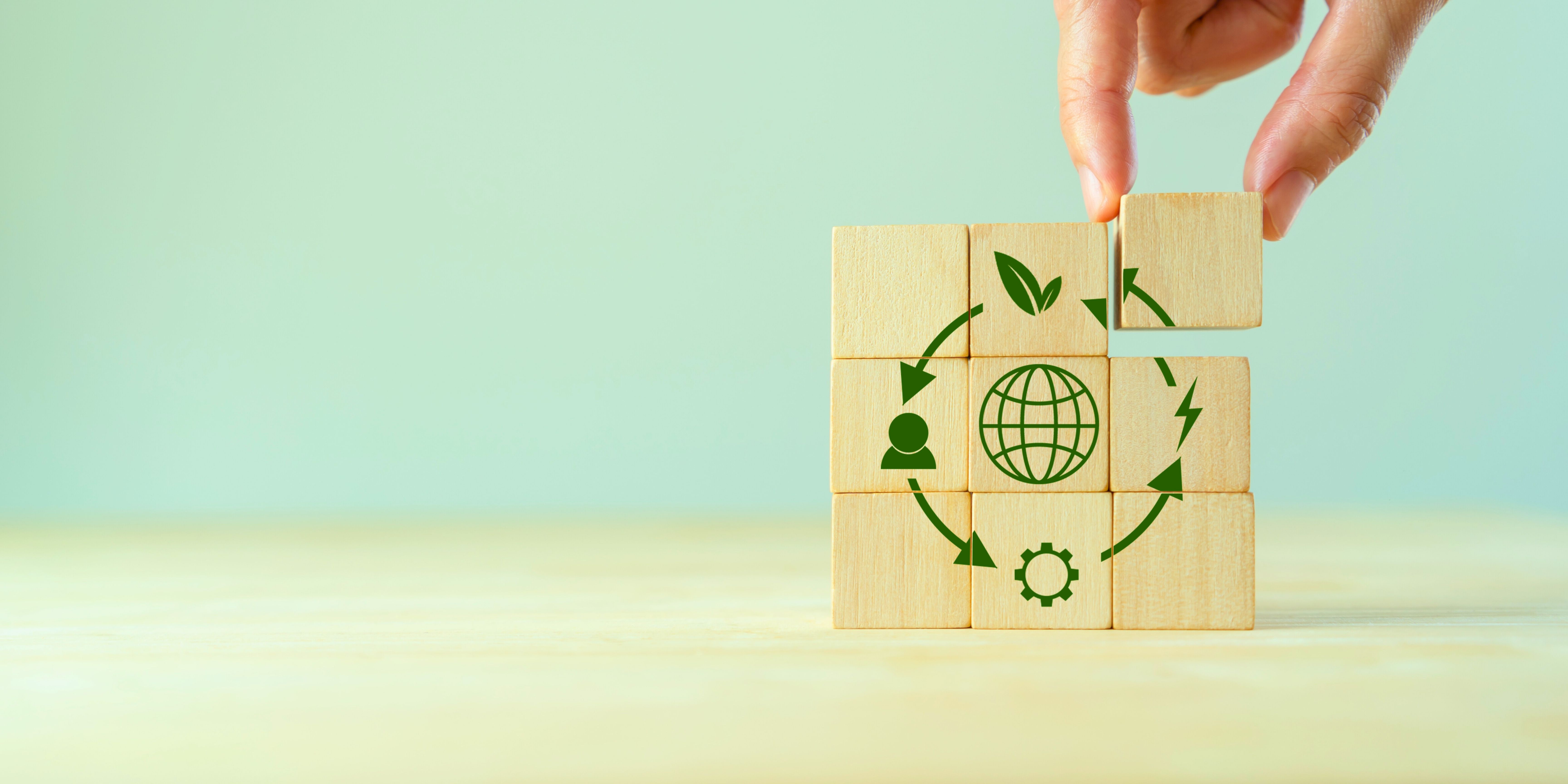 Close-up of a hand placing eco blocks with globe and recycling icons on a light wooden surface.
