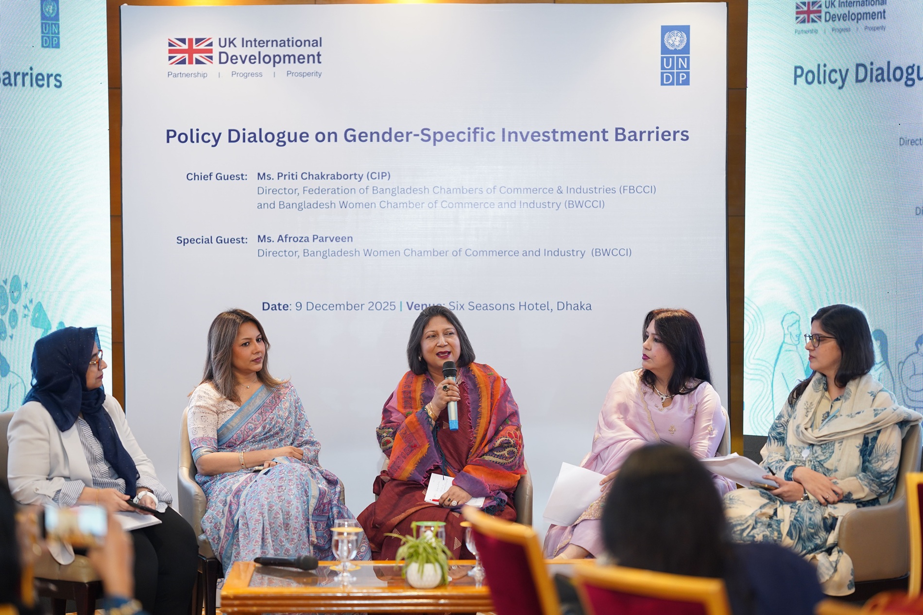 Five women panelists on stage during a policy discussion; banner behind them.