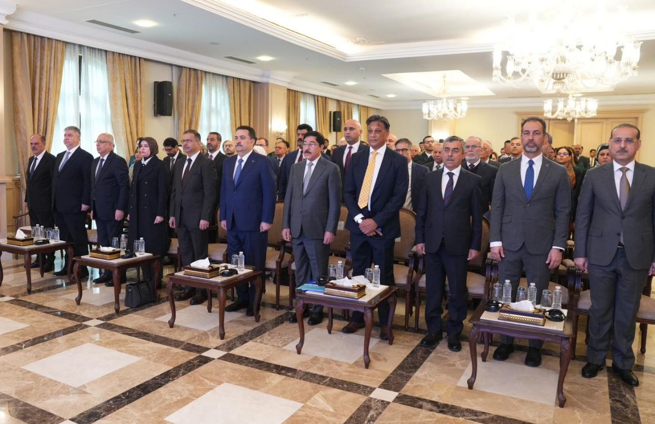 Group of men in suits standing in a formal meeting room with a chandelier.