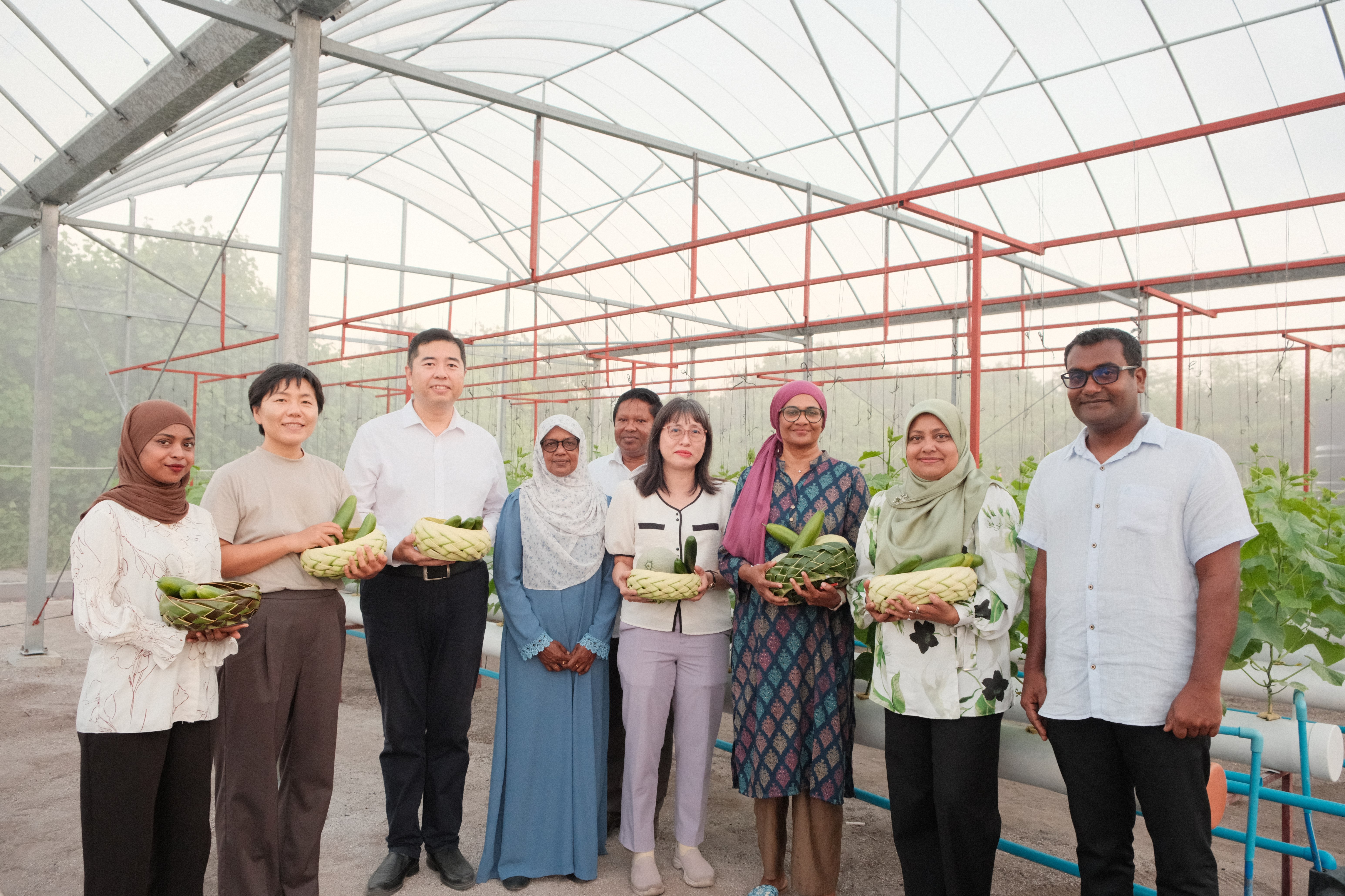 Group of diverse adults in a greenhouse, holding potted plants.