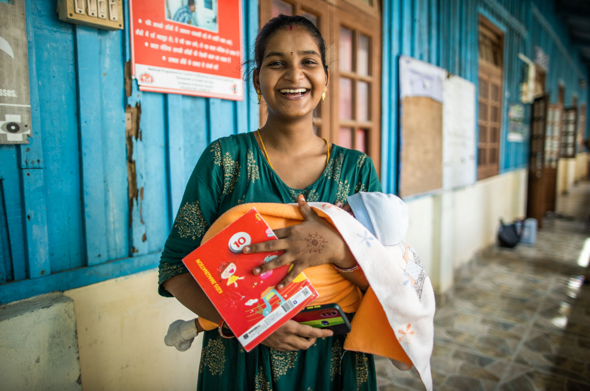 Photo of a person in a green striped shirt holding a red book beside a blue building.
