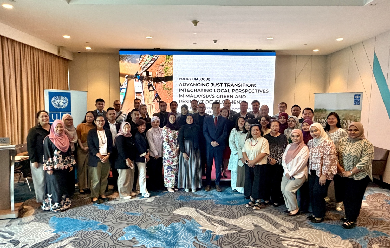 Group of professionals posing for a group photo in a conference room with banner and screen behind.
