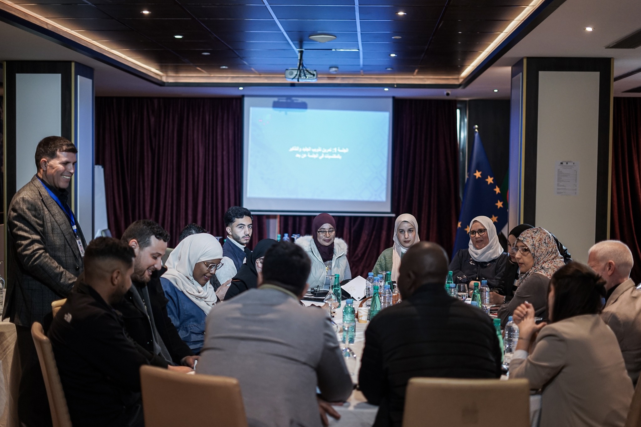 Group of people around a round table in a conference room with a projector screen.