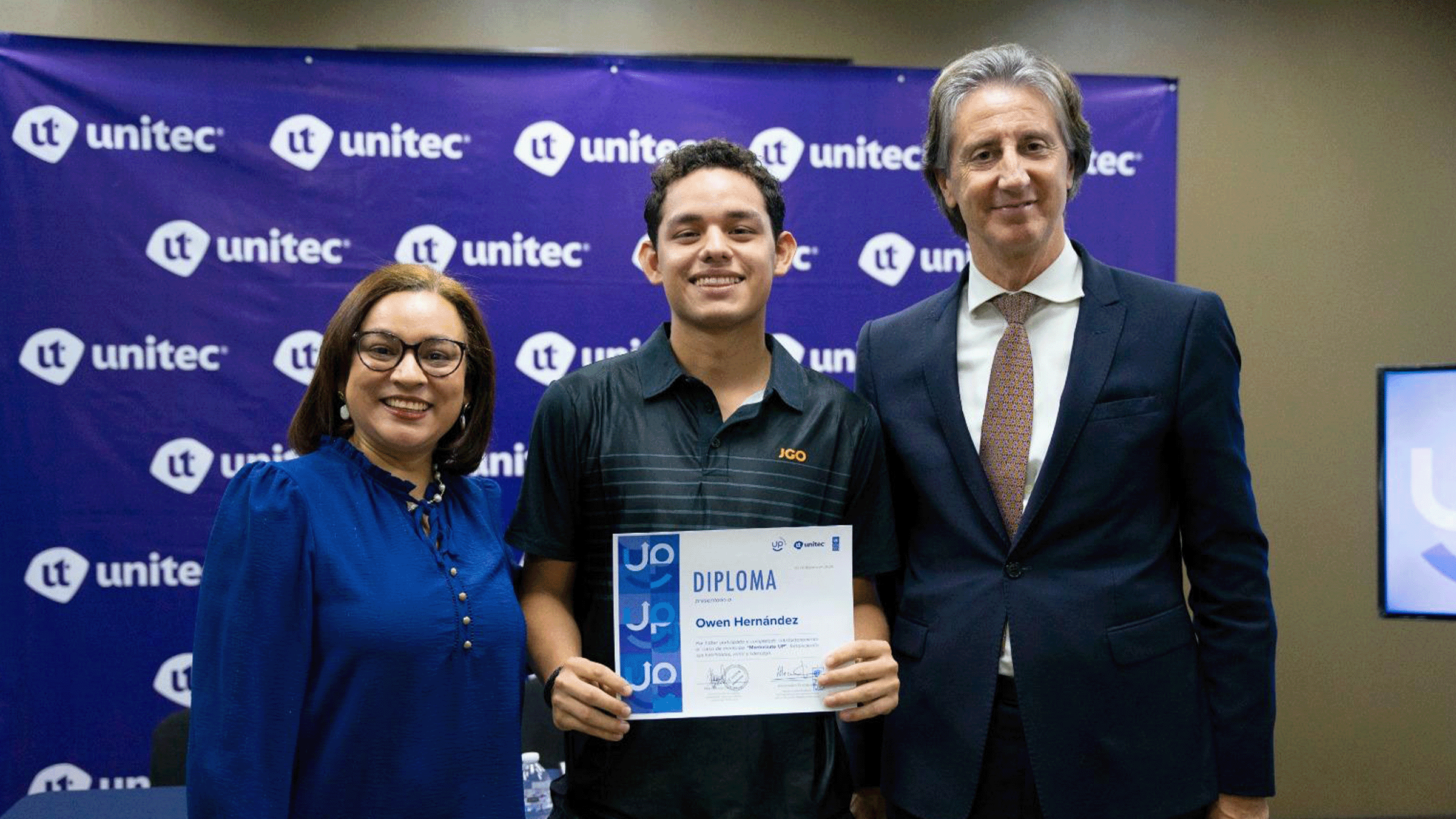 Three people pose with a certificate in front of a blue Unitec backdrop.