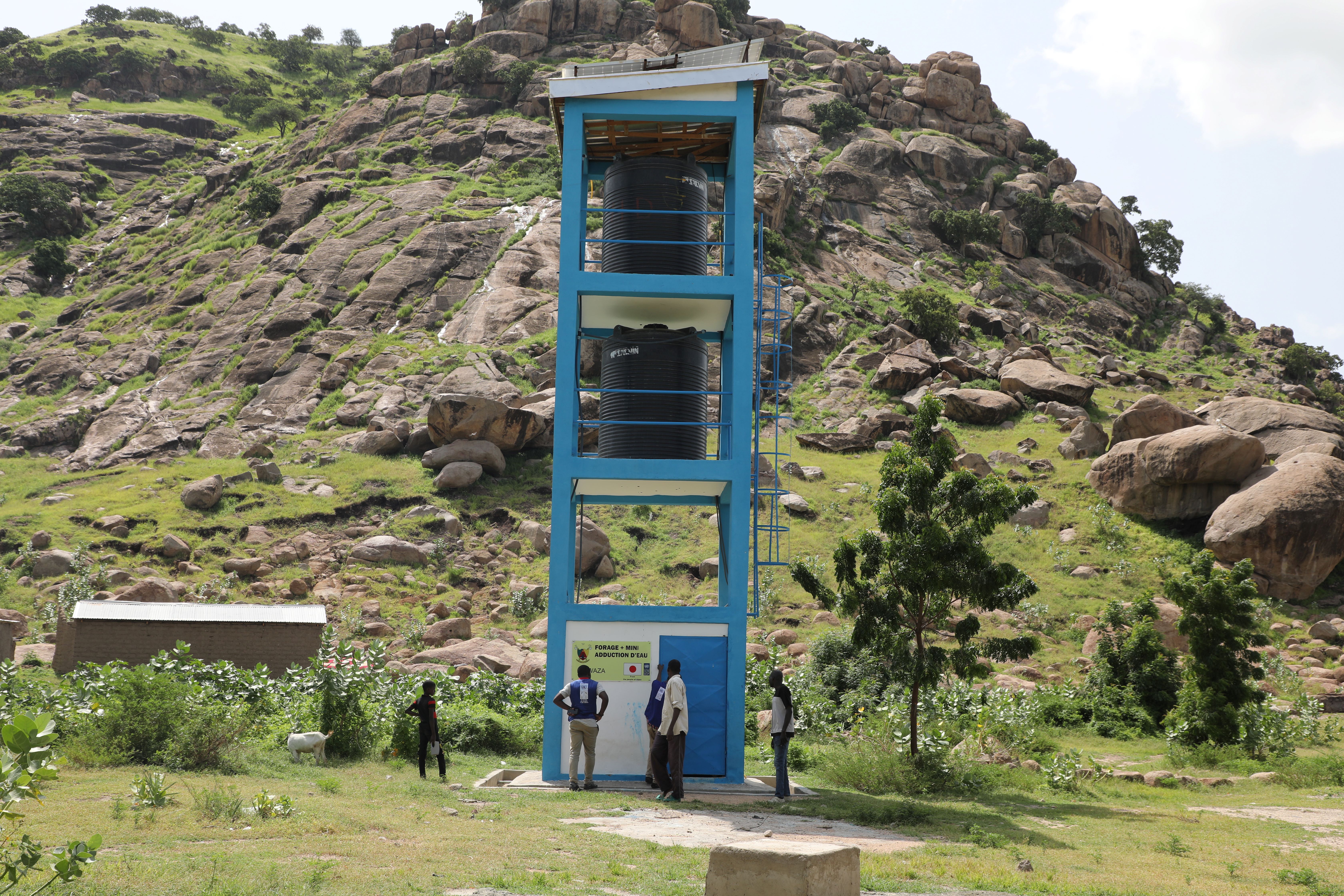 Photograph of a blue three-level metal tower in a grassy park; two people at its base.