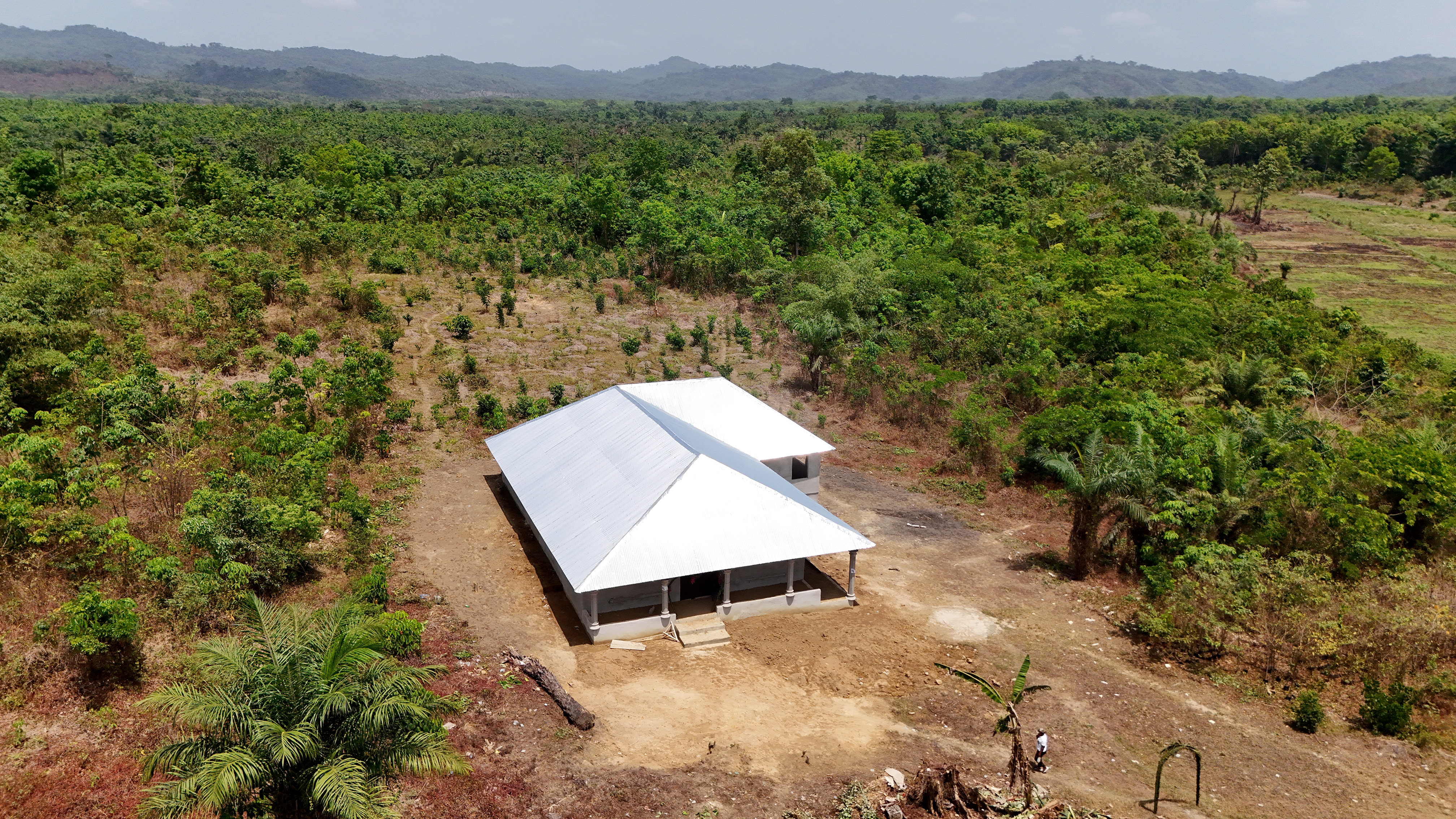 White canopy over a small shelter on a dirt field among young trees in a rural orchard.