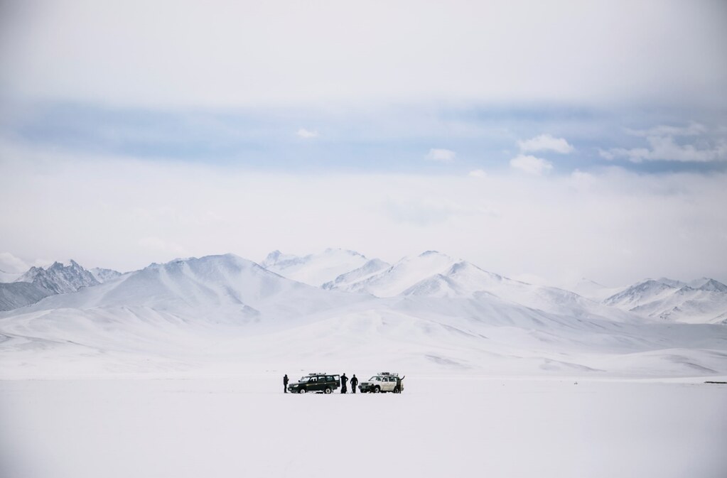 A small group of people on a snowy plain, with distant snow-capped mountains.