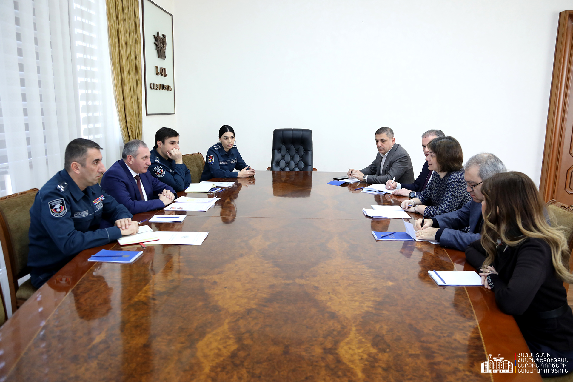 Officials seated along a long wooden conference table with documents, in a bright meeting room.