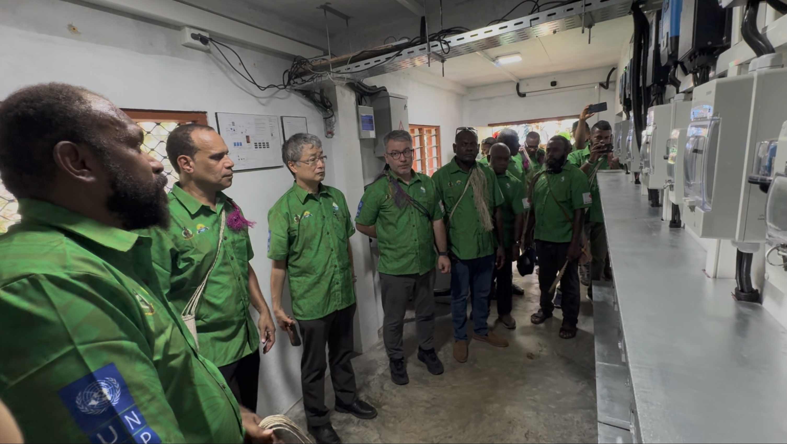 Group of people in green uniforms standing in a workshop, listening to a guide.