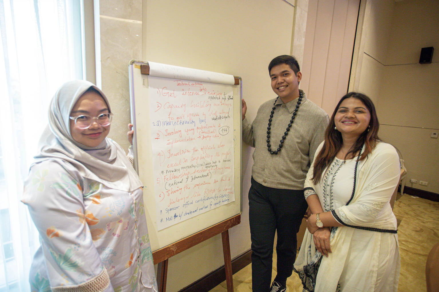 Three people stand around a whiteboard with handwritten notes in a classroom.
