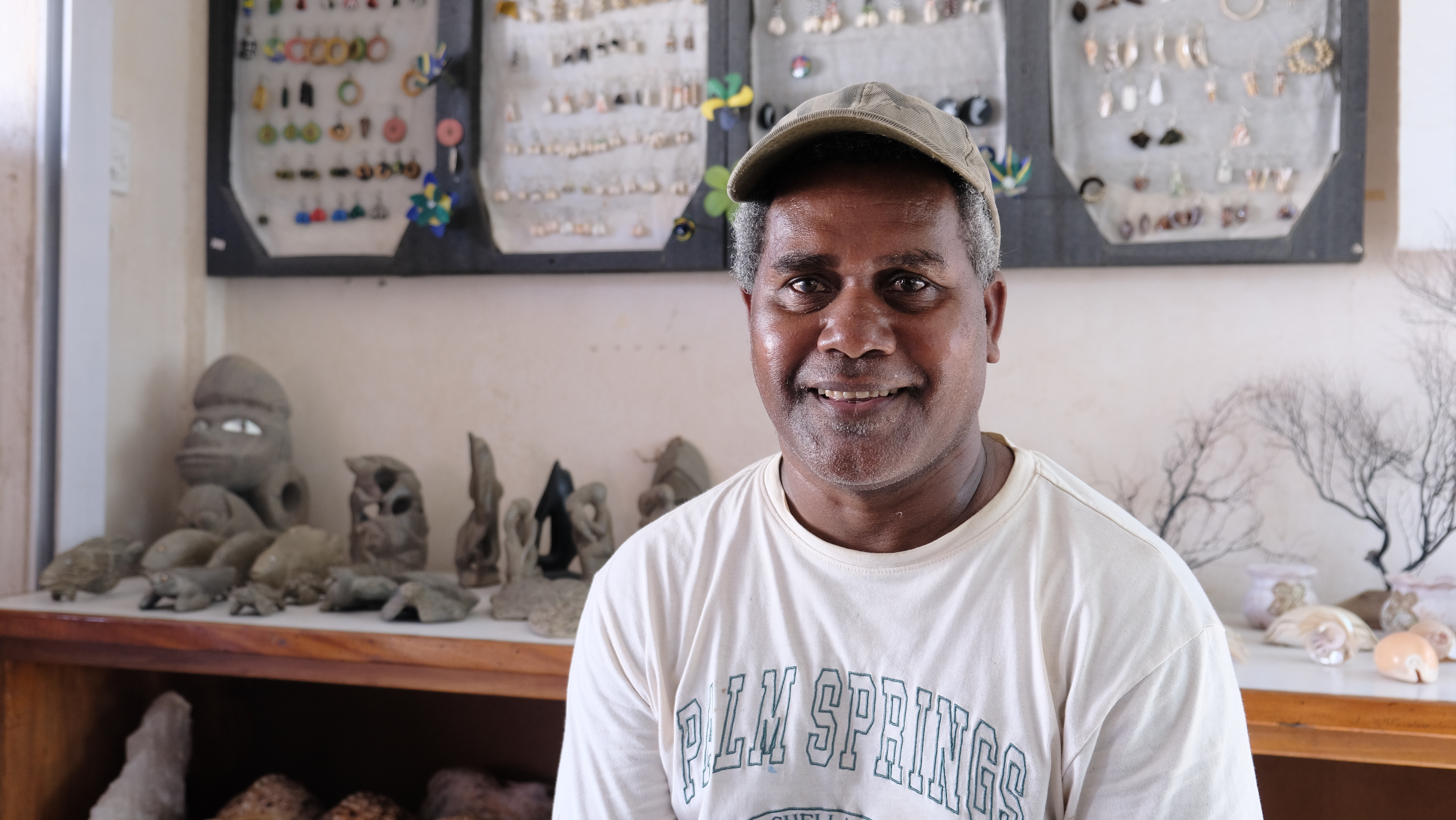 Person in a white T-shirt stands in a room with wooden shelves and ceramic owl figurines.