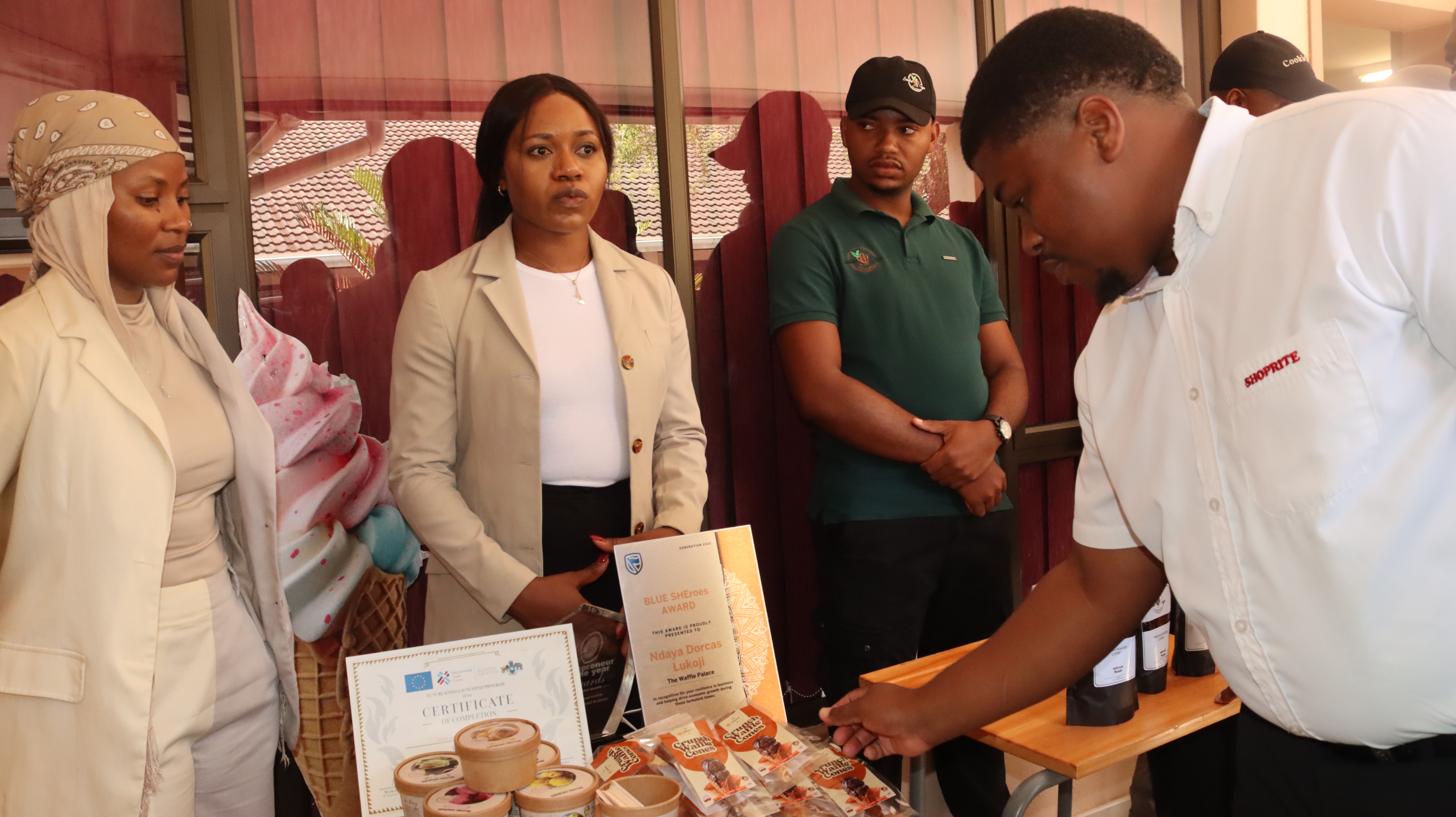 Group of people at a food stall examining pastries on a table under pink tents.