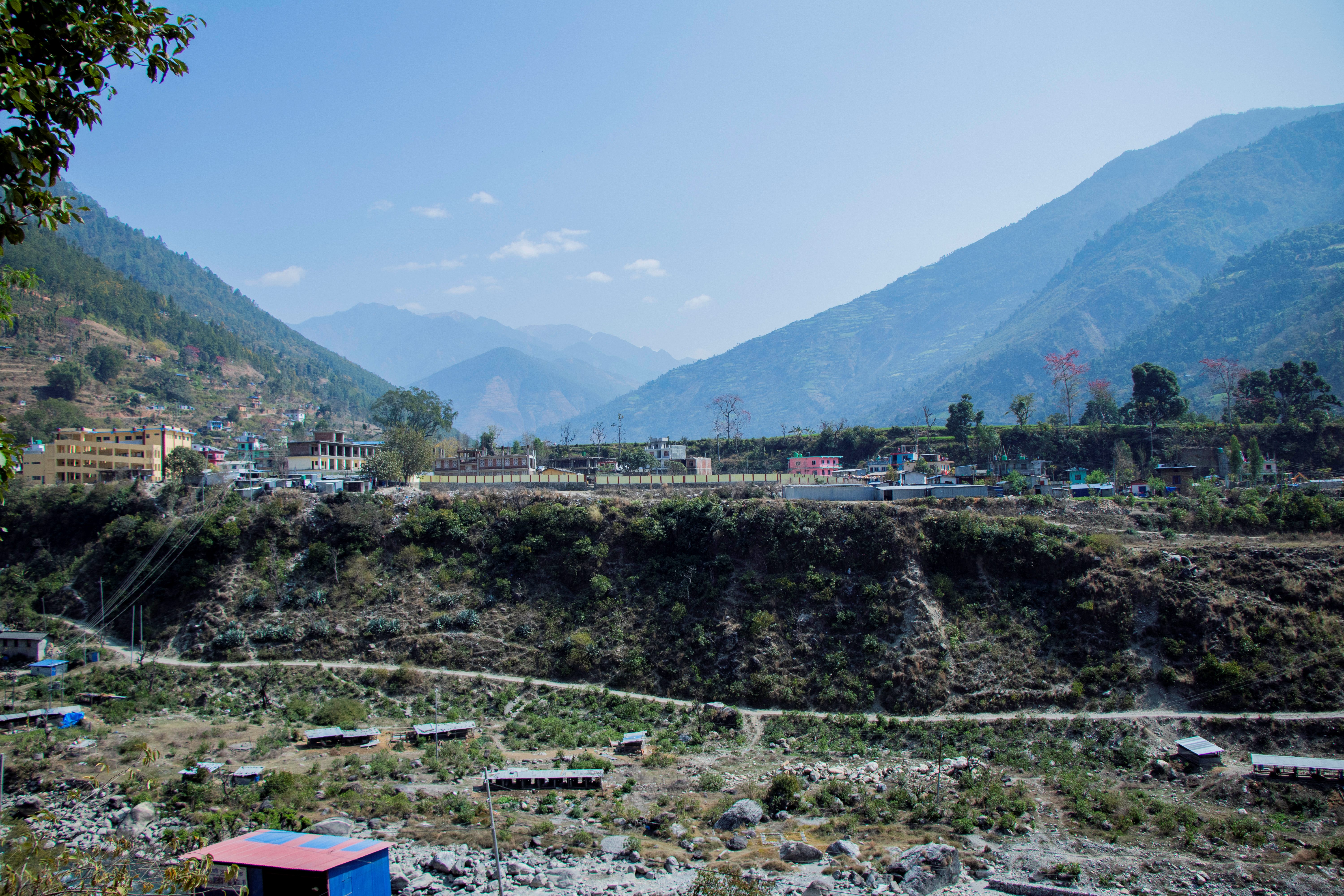 Terraced valley with stone walls in foreground, hillside village, blue mountains under clear sky.