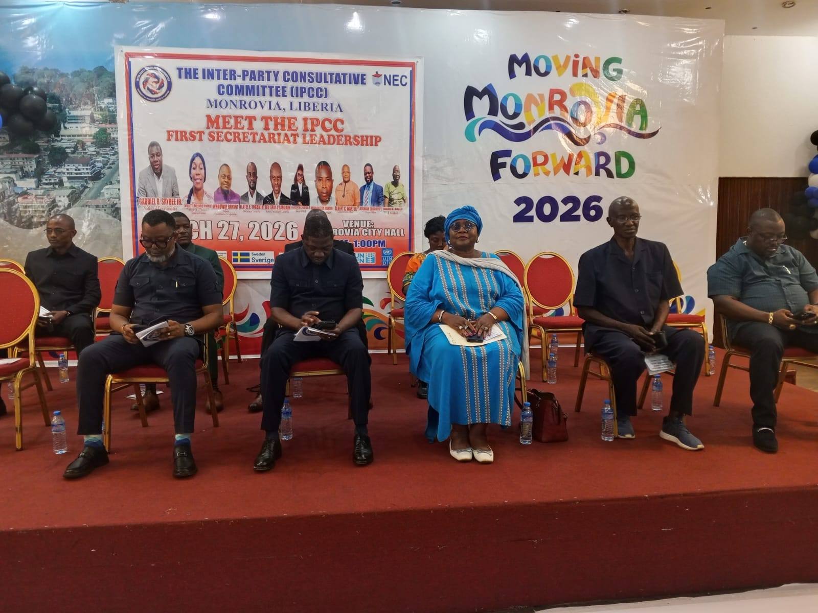 Photo of a panel discussion with seven people seated on a stage, banners behind them.