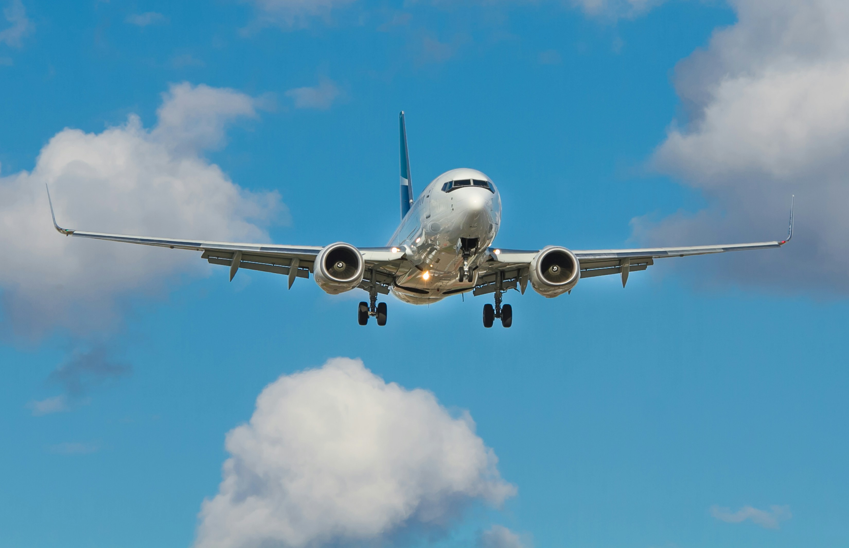 Front view of a commercial airliner approaching with landing gear down against a blue sky.