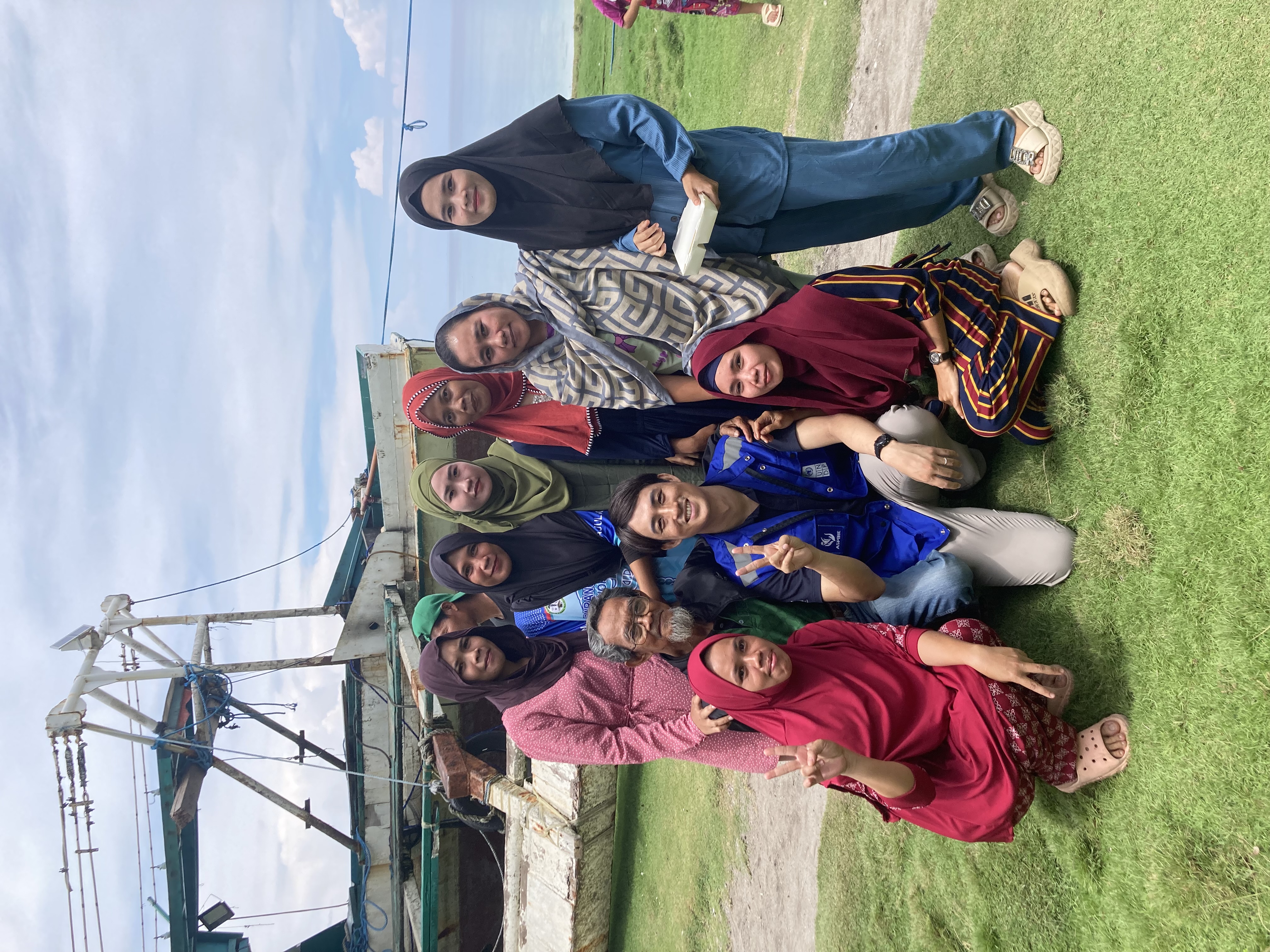 Group of diverse people posing outdoors on grass near a skate park.