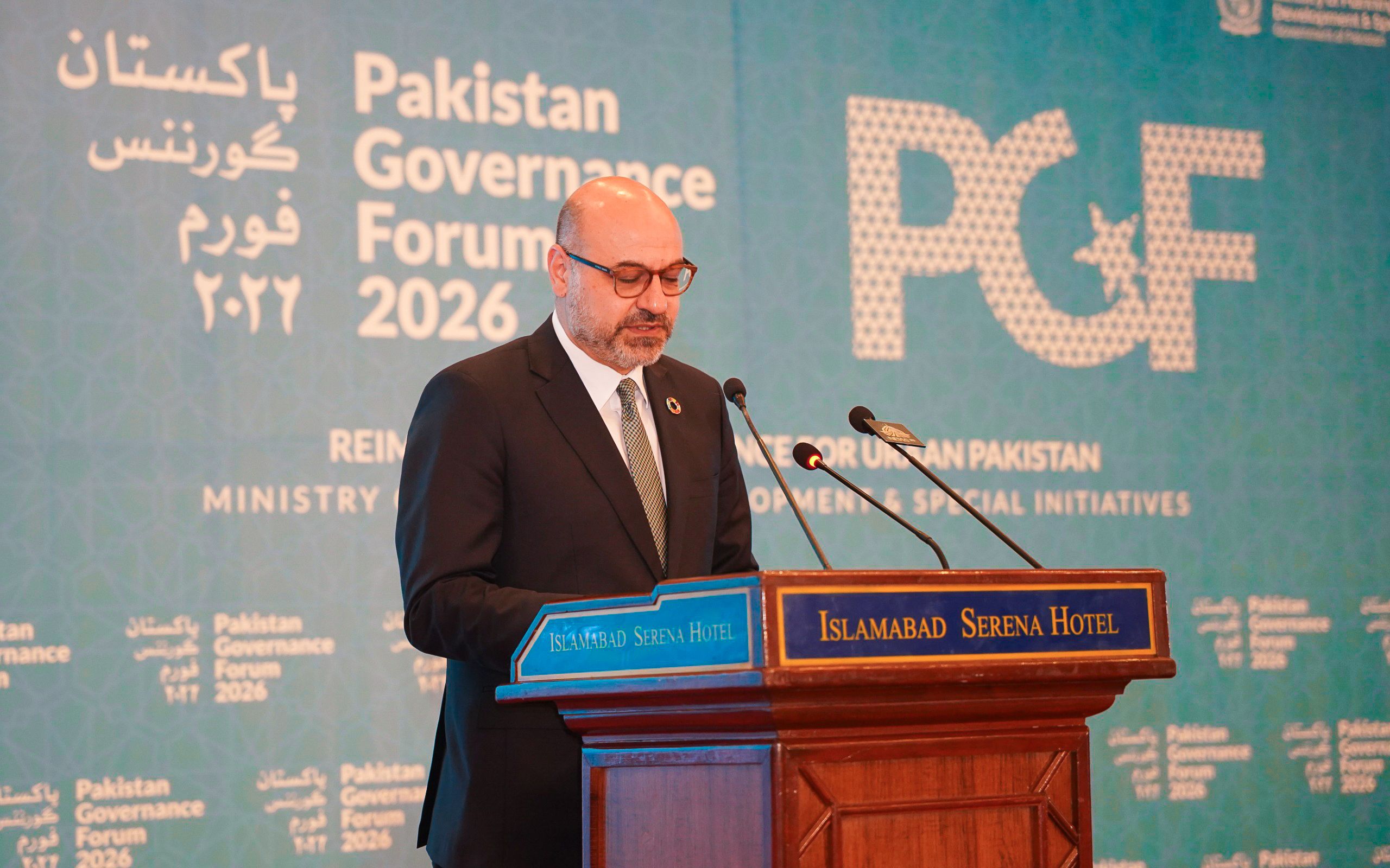 Photograph of a speaker at a podium against a blue backdrop with Pakistan Government Forum banners.