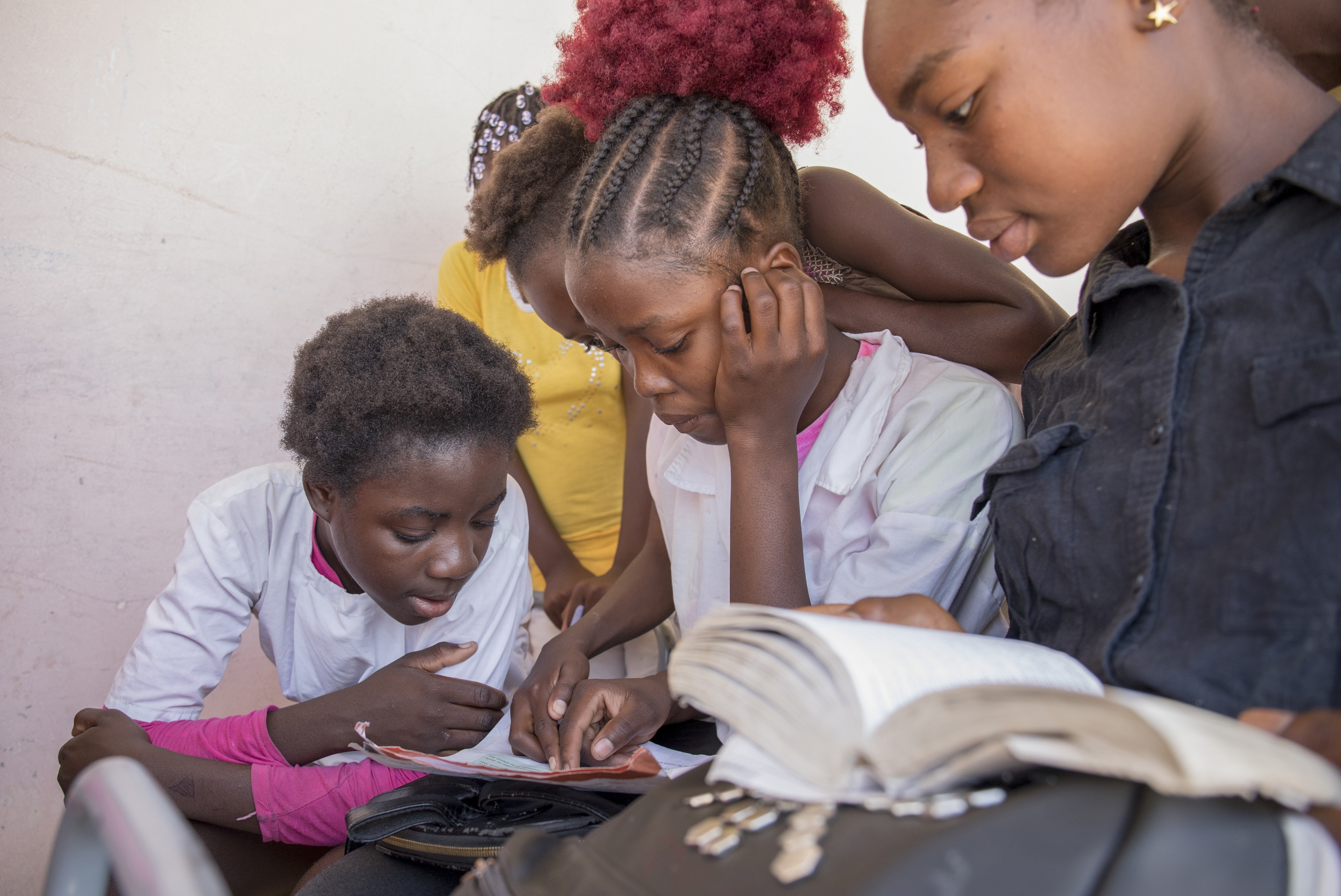 Three people studying around an open book in a bright room.