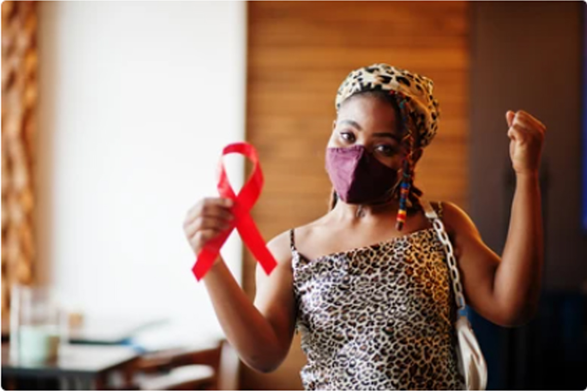 Person in leopard-print top holds a red awareness ribbon, fist raised, in a home.