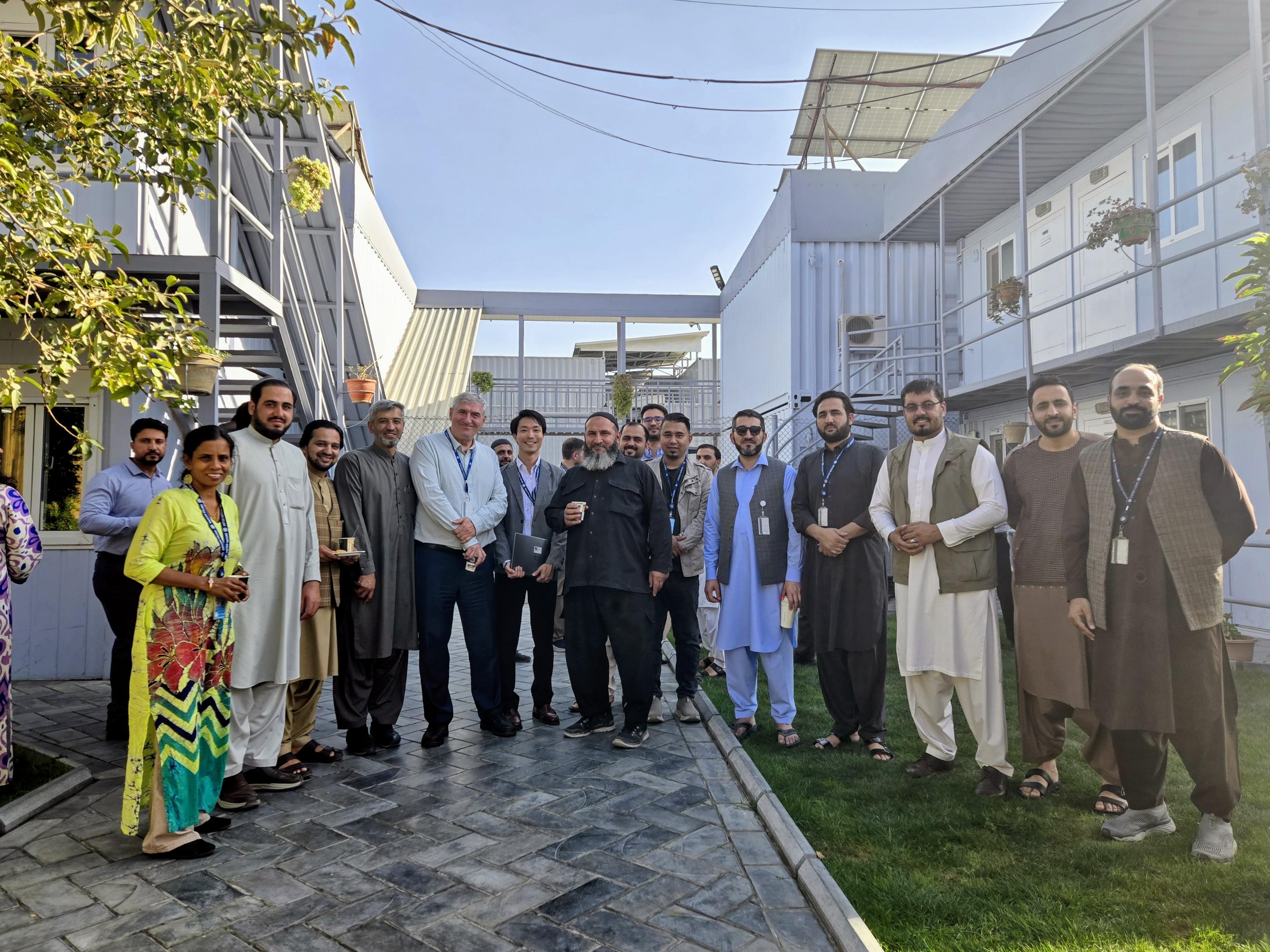 Photograph: Group of people posing outdoors in a sunny courtyard between light-blue buildings.