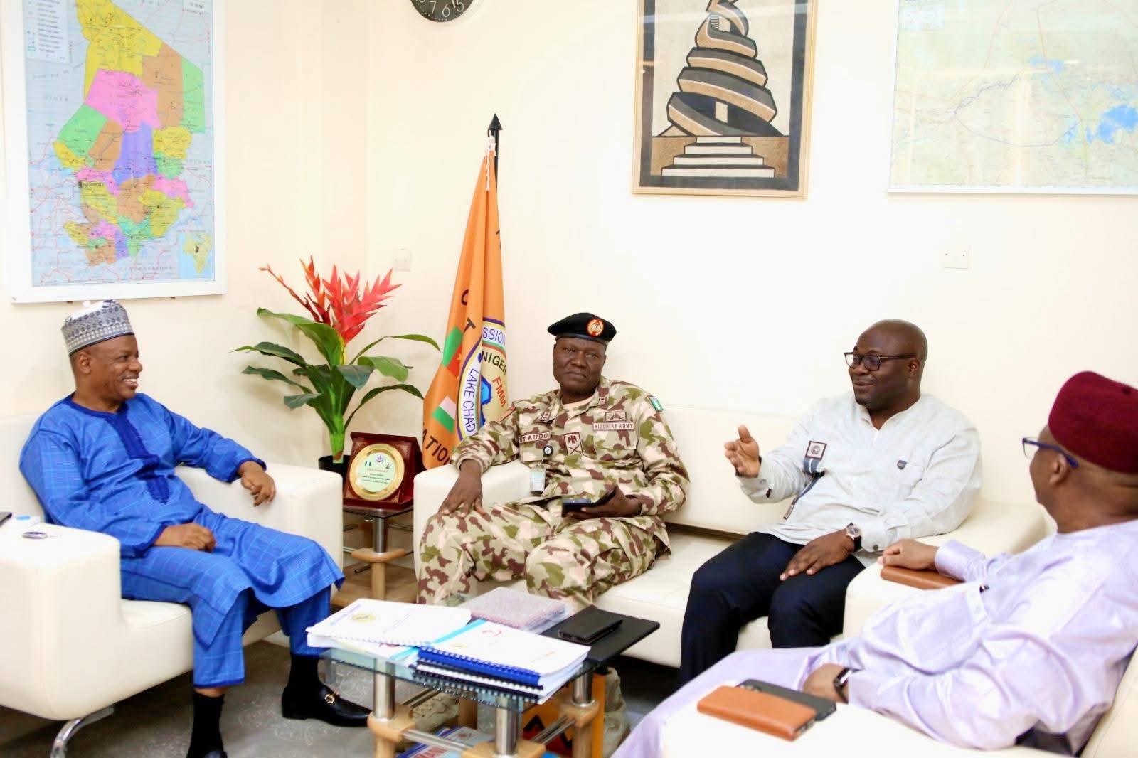 Five men in traditional and formal attire sit in a bright office around a glass coffee table.