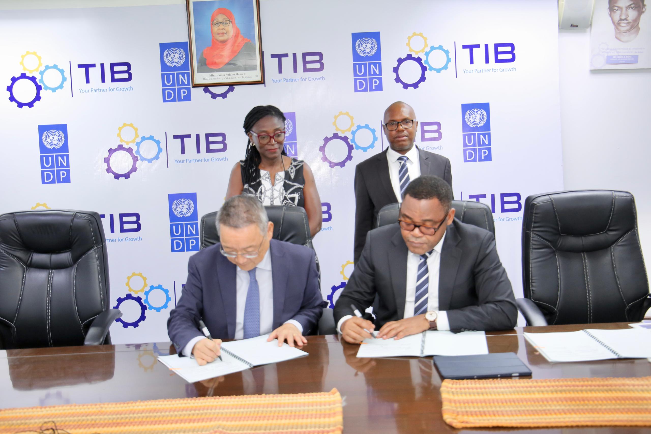 Two men signing documents at a table while two people stand behind; backdrop with TIB logos.